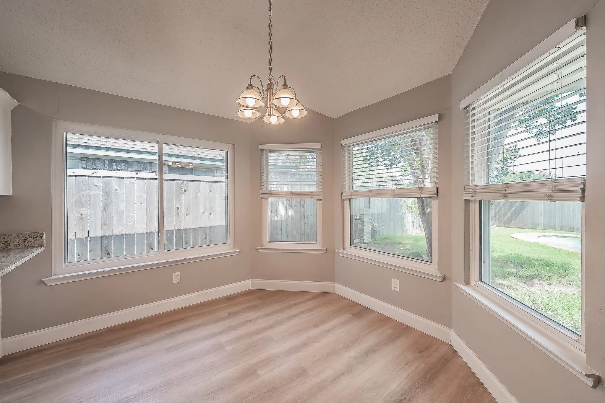 Bay window area featuring wood-finish flooring, a contemporary chandelier, and multiple windows with blinds