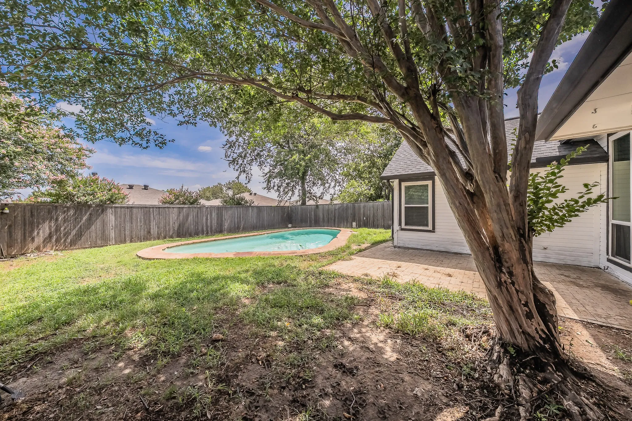 Expansive backyard featuring a fenced perimeter, a mature shade tree, a swimming pool with a stone coping, and a paved patio area