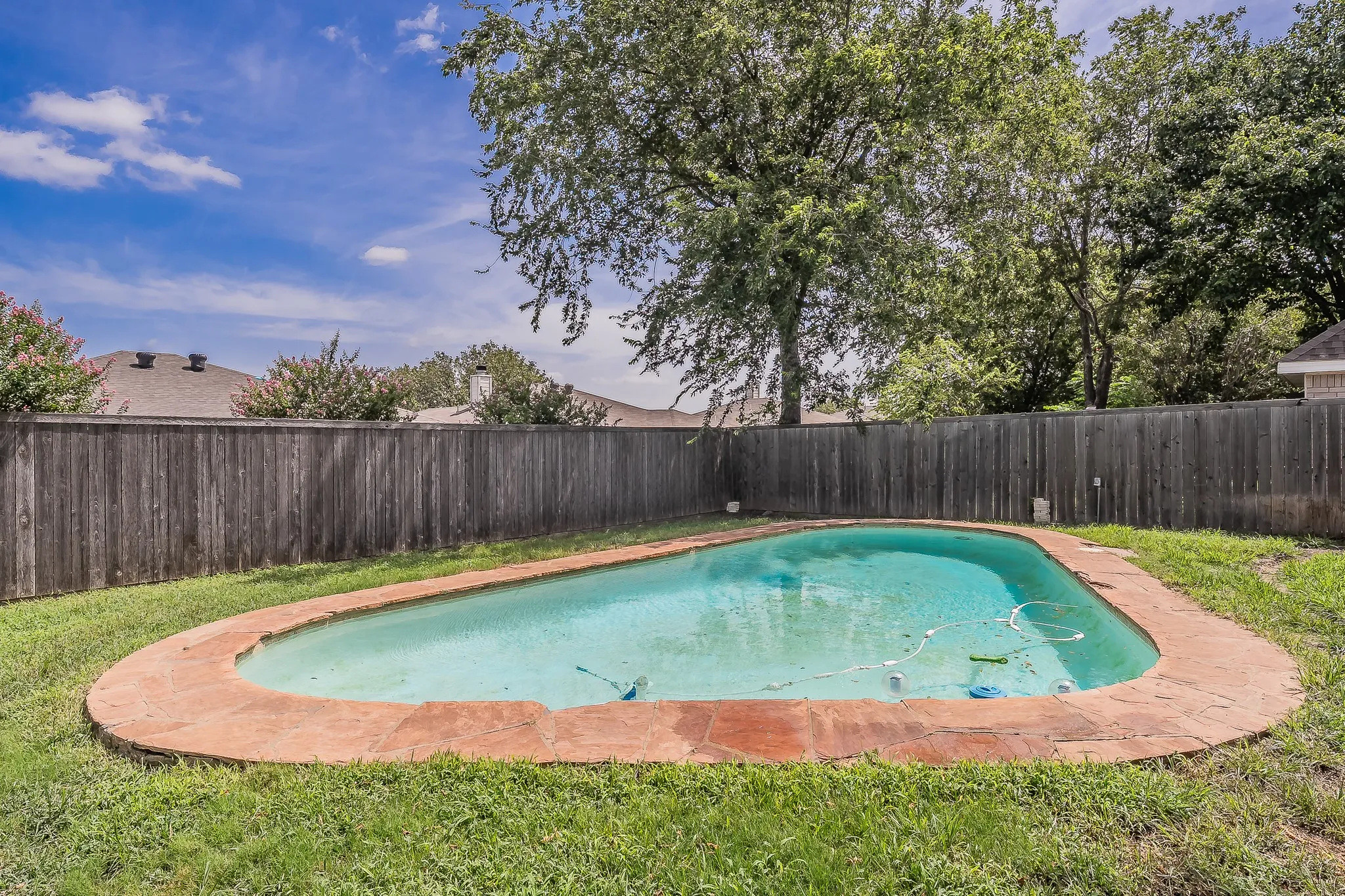 Freeform swimming pool with a flagstone coping, surrounded by a wooden privacy fence and green lawn