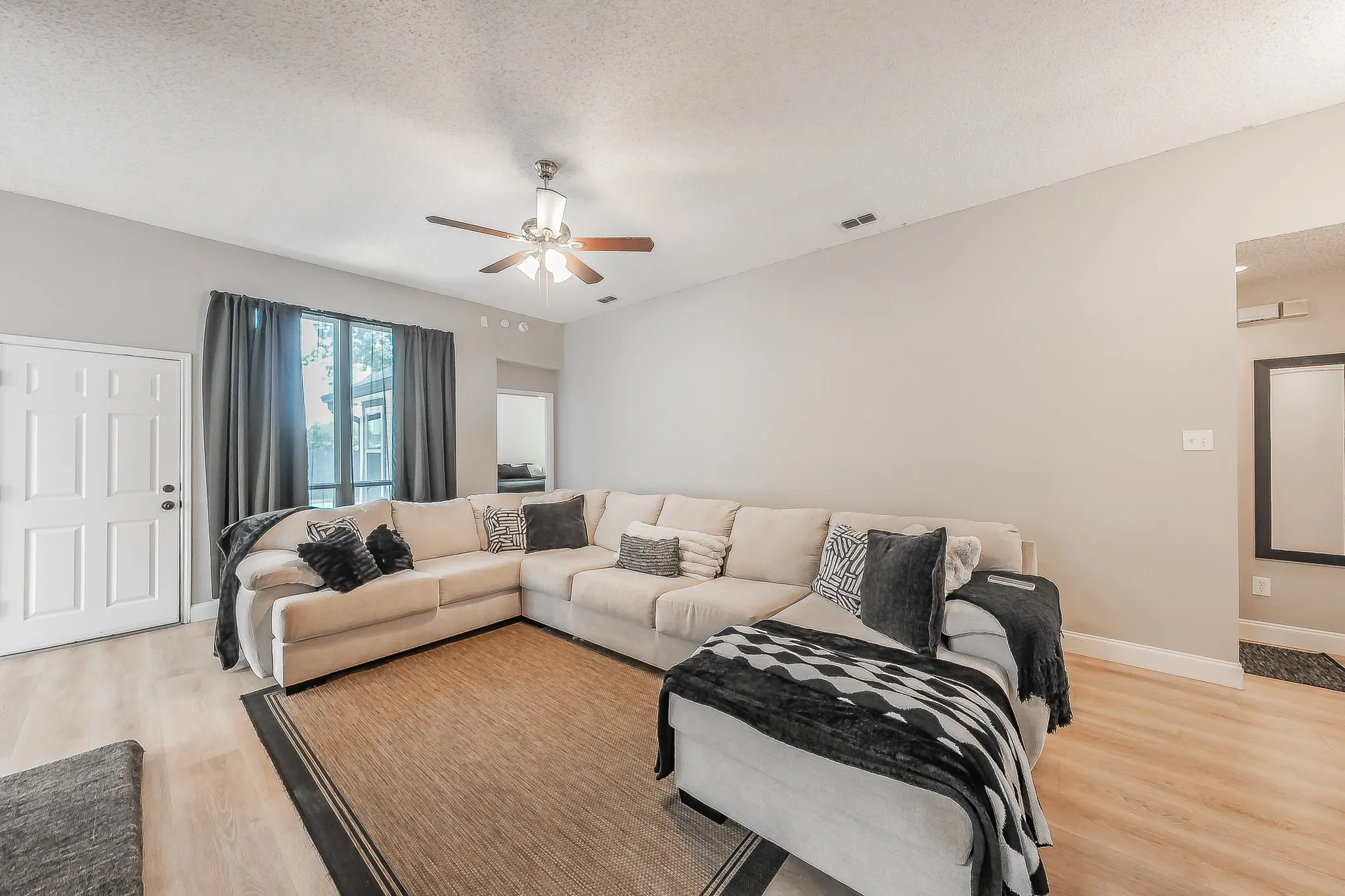 Spacious living area featuring light wood-finish flooring, neutral wall tones, and a ceiling fan with integrated lighting