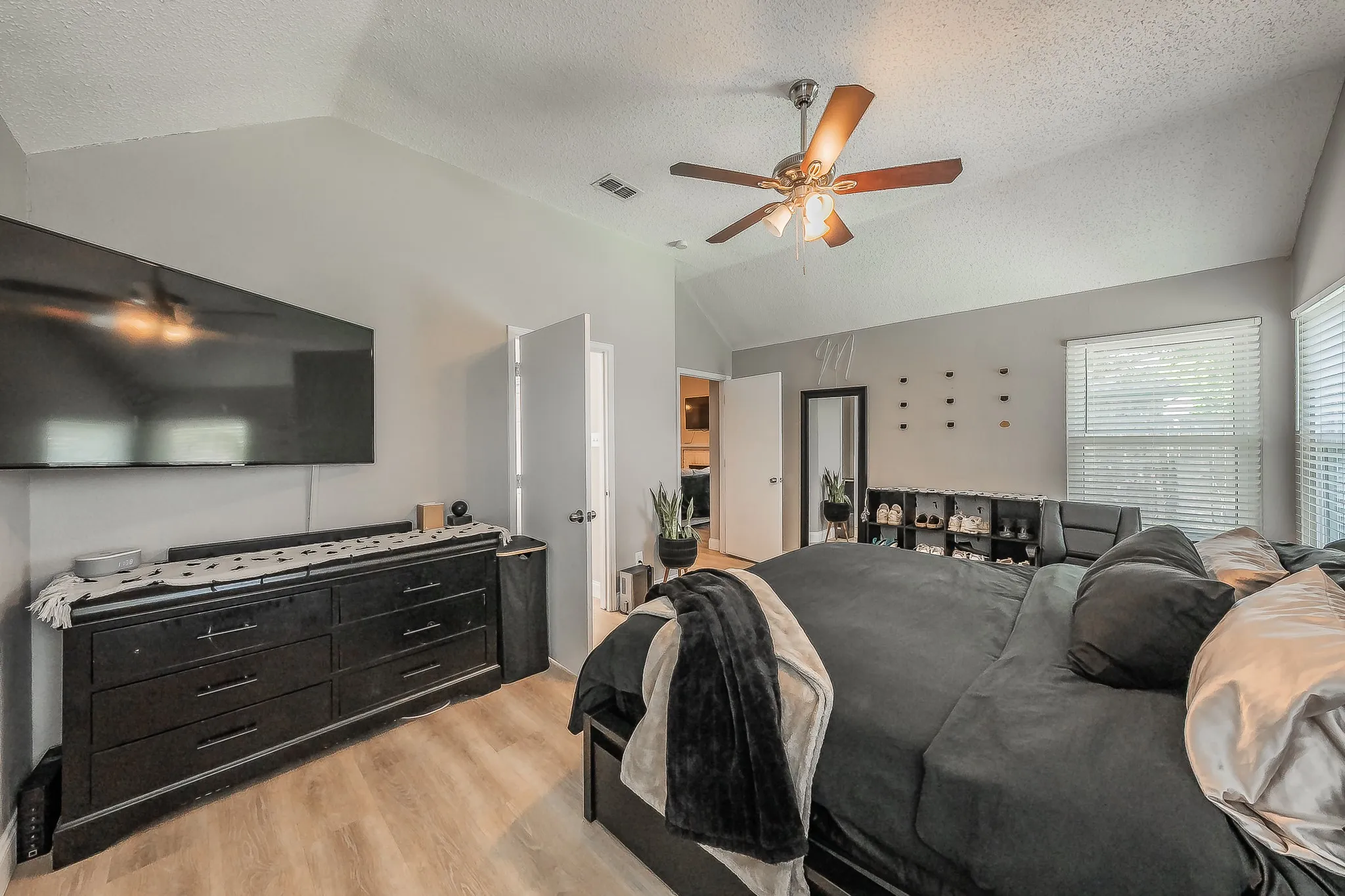 Vaulted ceiling bedroom featuring wood-finish flooring, a ceiling fan with light fixture, and horizontal blinds on windows