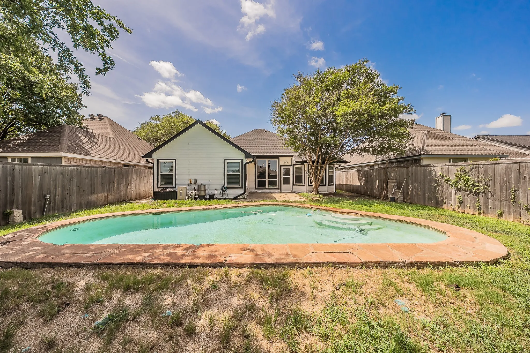 Backyard featuring a freeform swimming pool with stone coping, a private wood fence, and mature trees