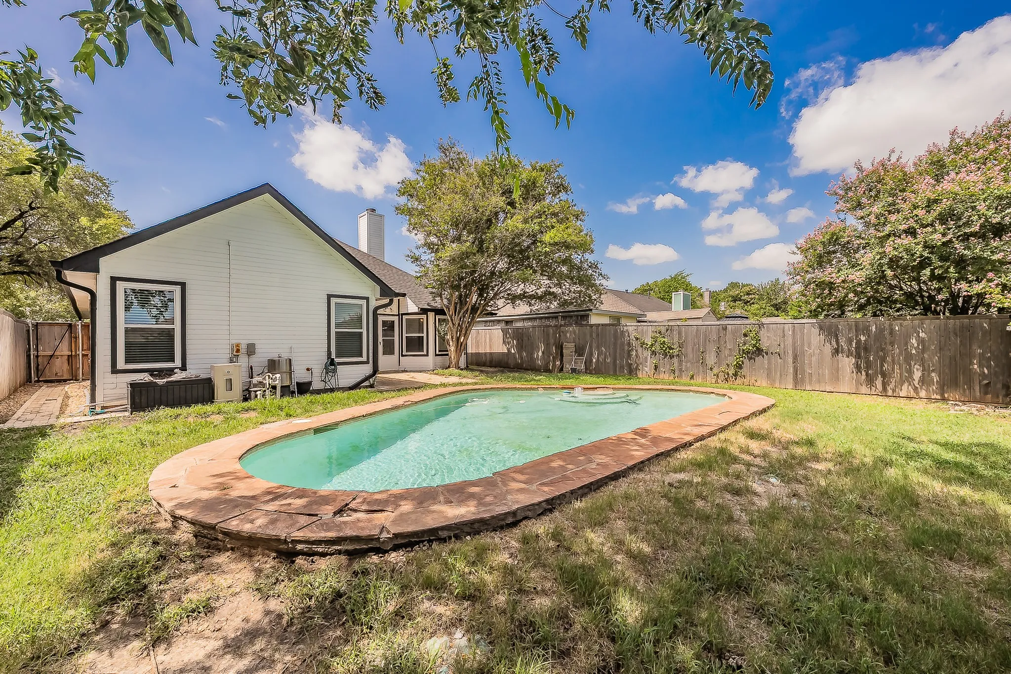 Backyard oasis featuring an in-ground swimming pool with stone coping, surrounded by a grassy lawn and mature trees