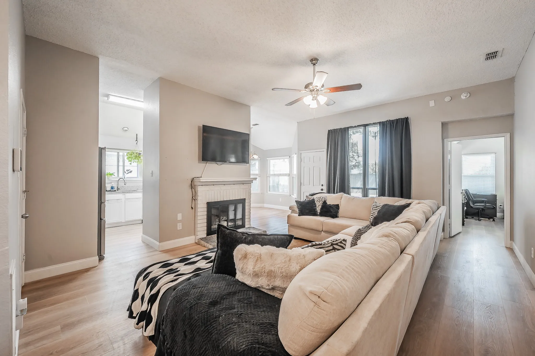 Open-concept living area with wood-finish flooring, a white brick fireplace, and a ceiling fan