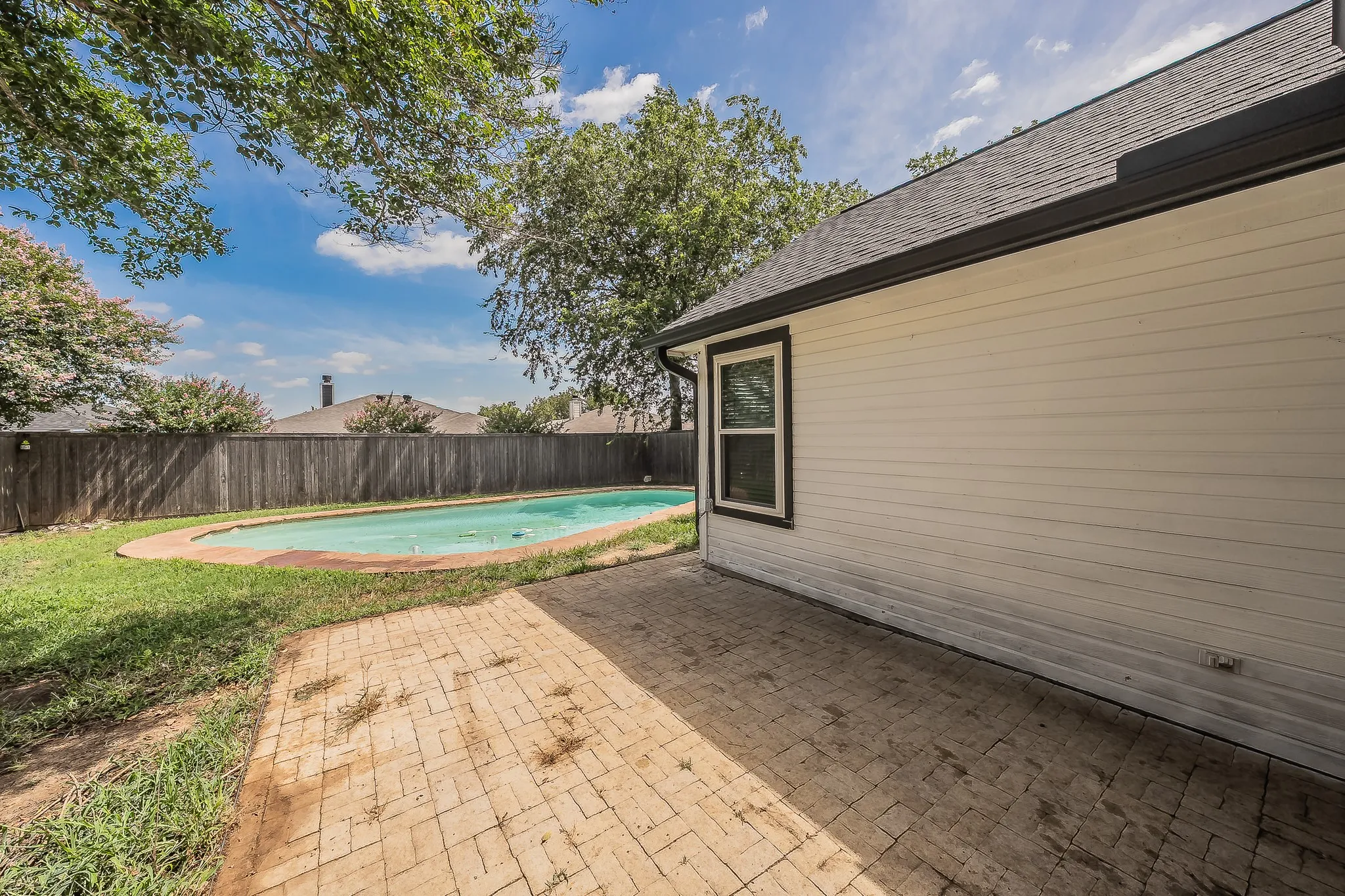 Backyard featuring an in-ground swimming pool, a brick paver patio, a wood privacy fence, and mature trees