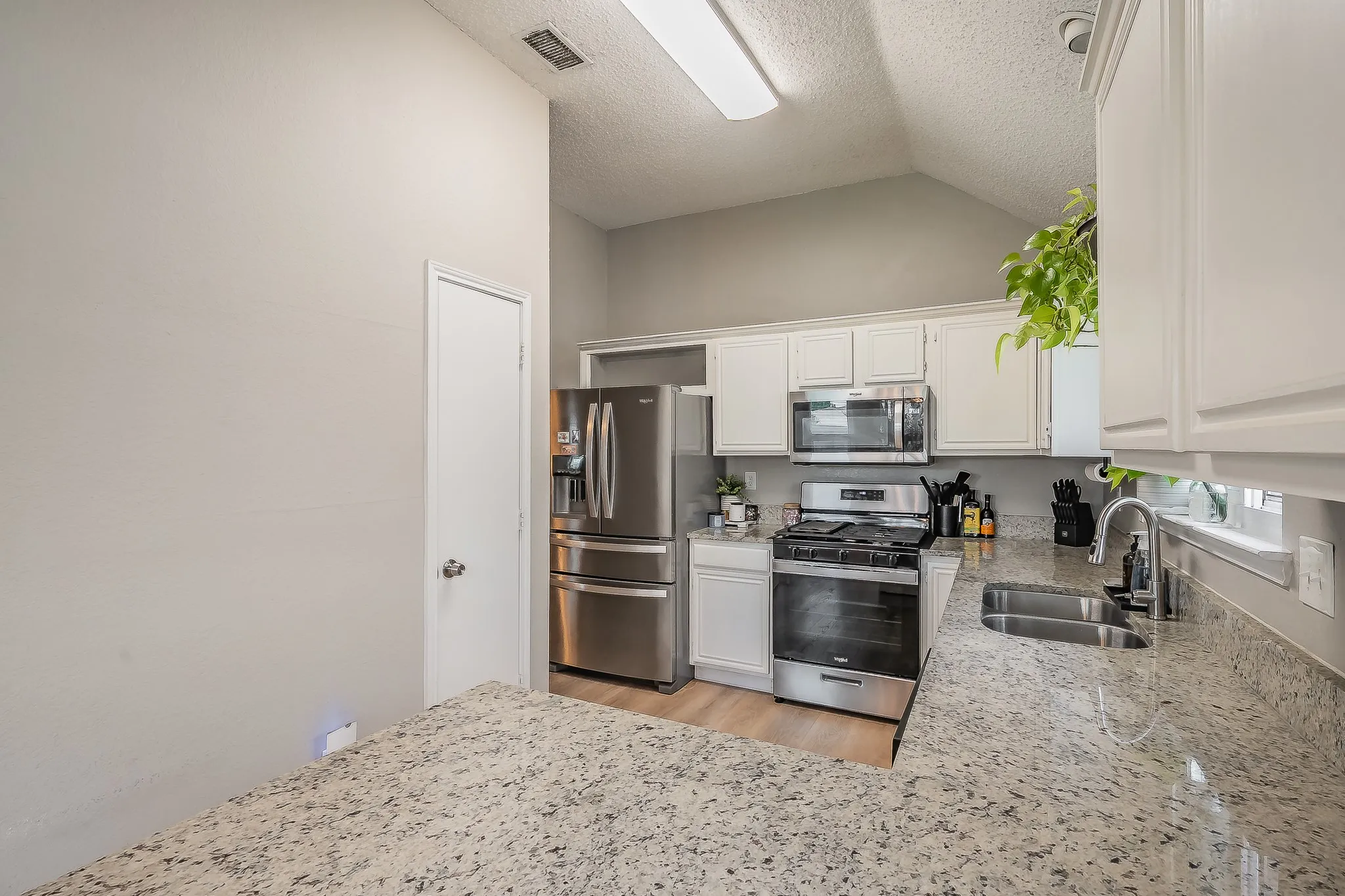 Kitchen featuring granite countertops, white cabinetry, stainless steel appliances, a double basin sink, and a vaulted ceiling