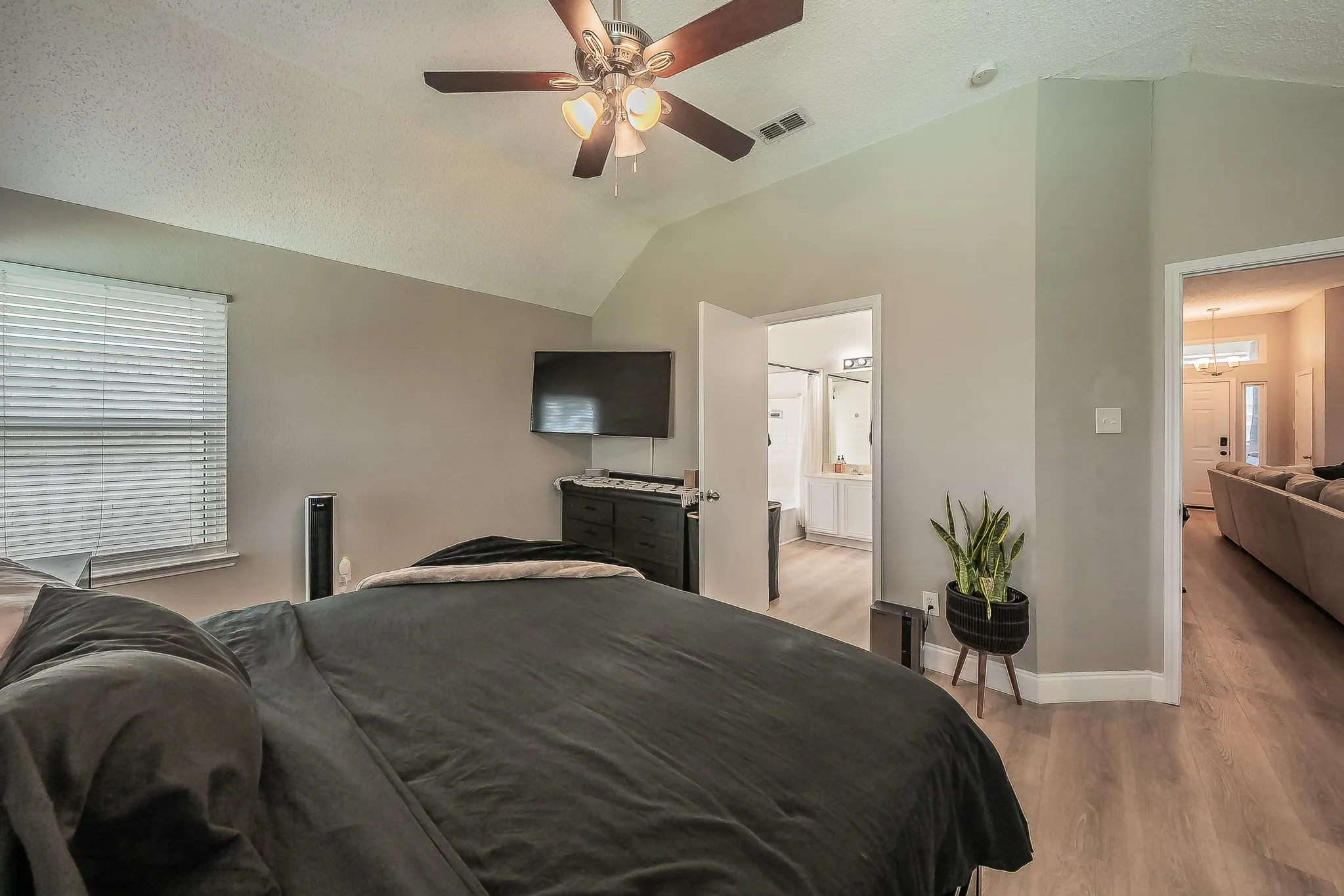 Vaulted ceiling with a ceiling fan, light wood-finish flooring, and a window with horizontal blinds