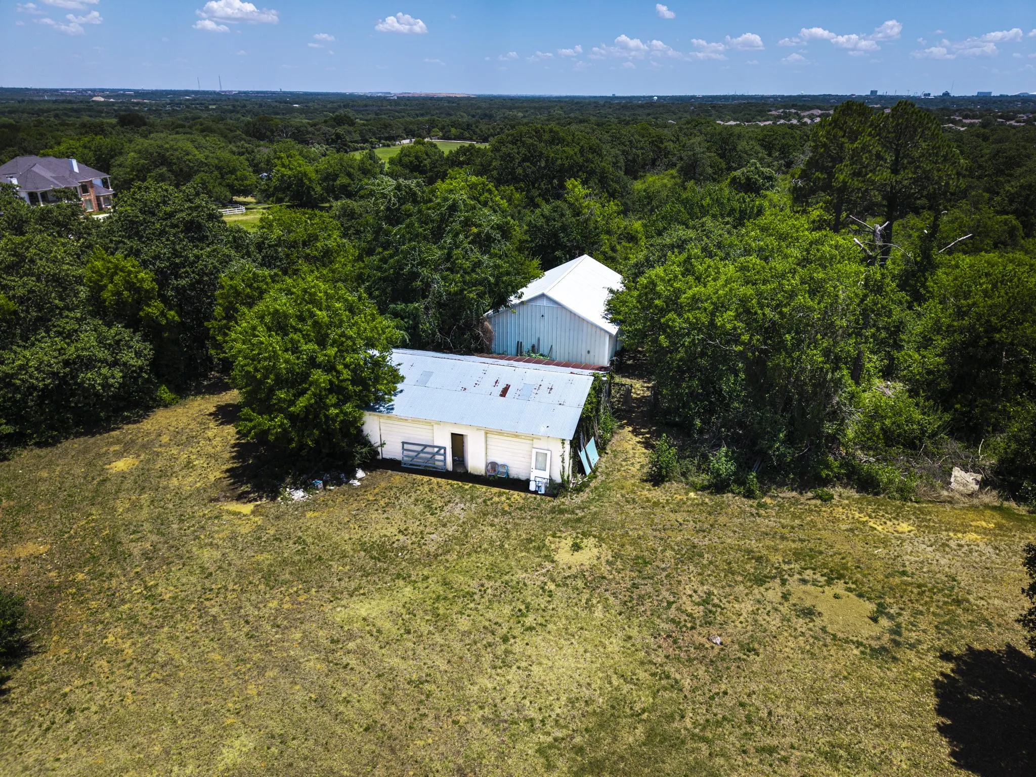 Expansive treed lot featuring two white-sided outbuildings with metal roofs