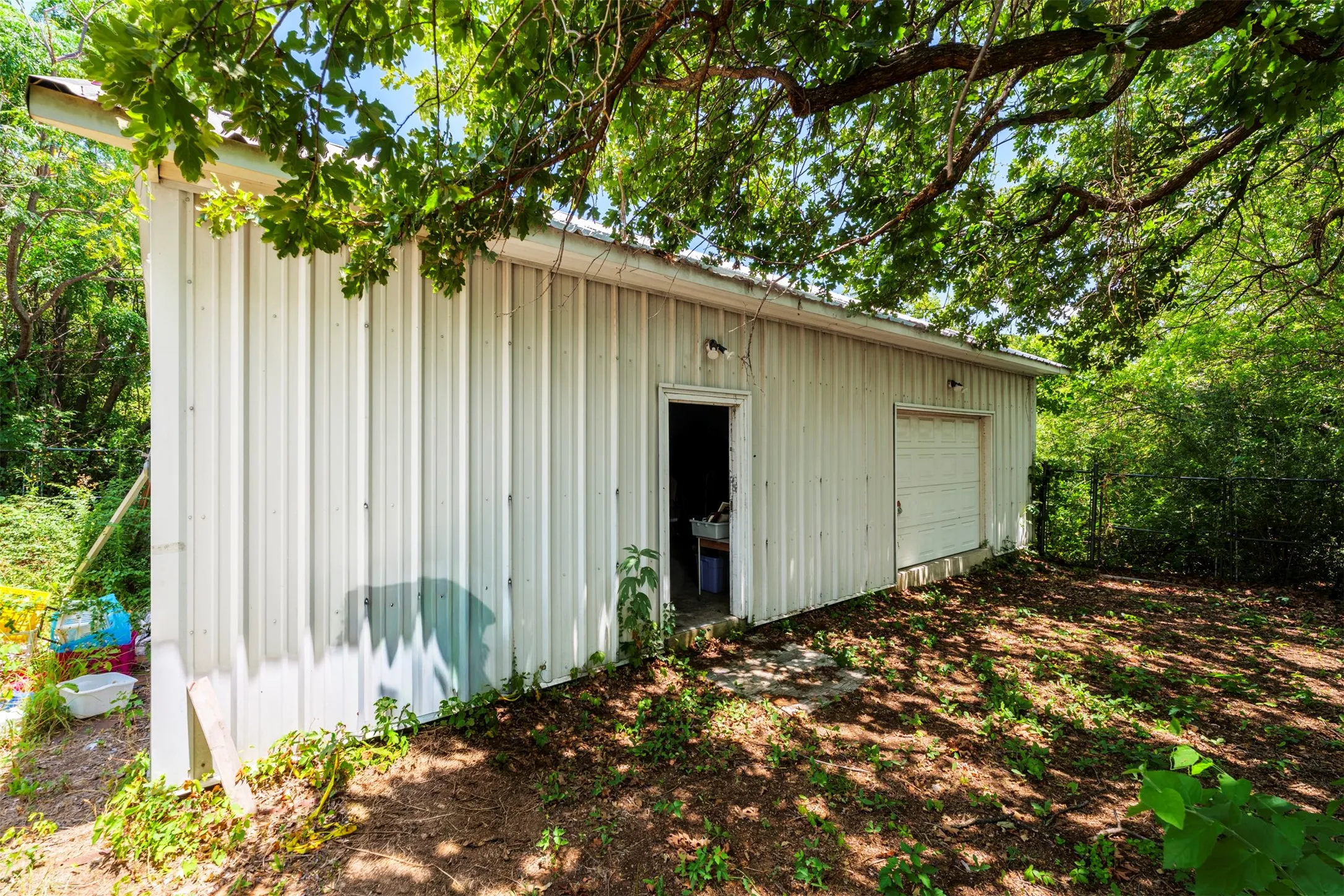 Metal-sided outbuilding featuring a single garage door, a pedestrian door, and exterior lighting