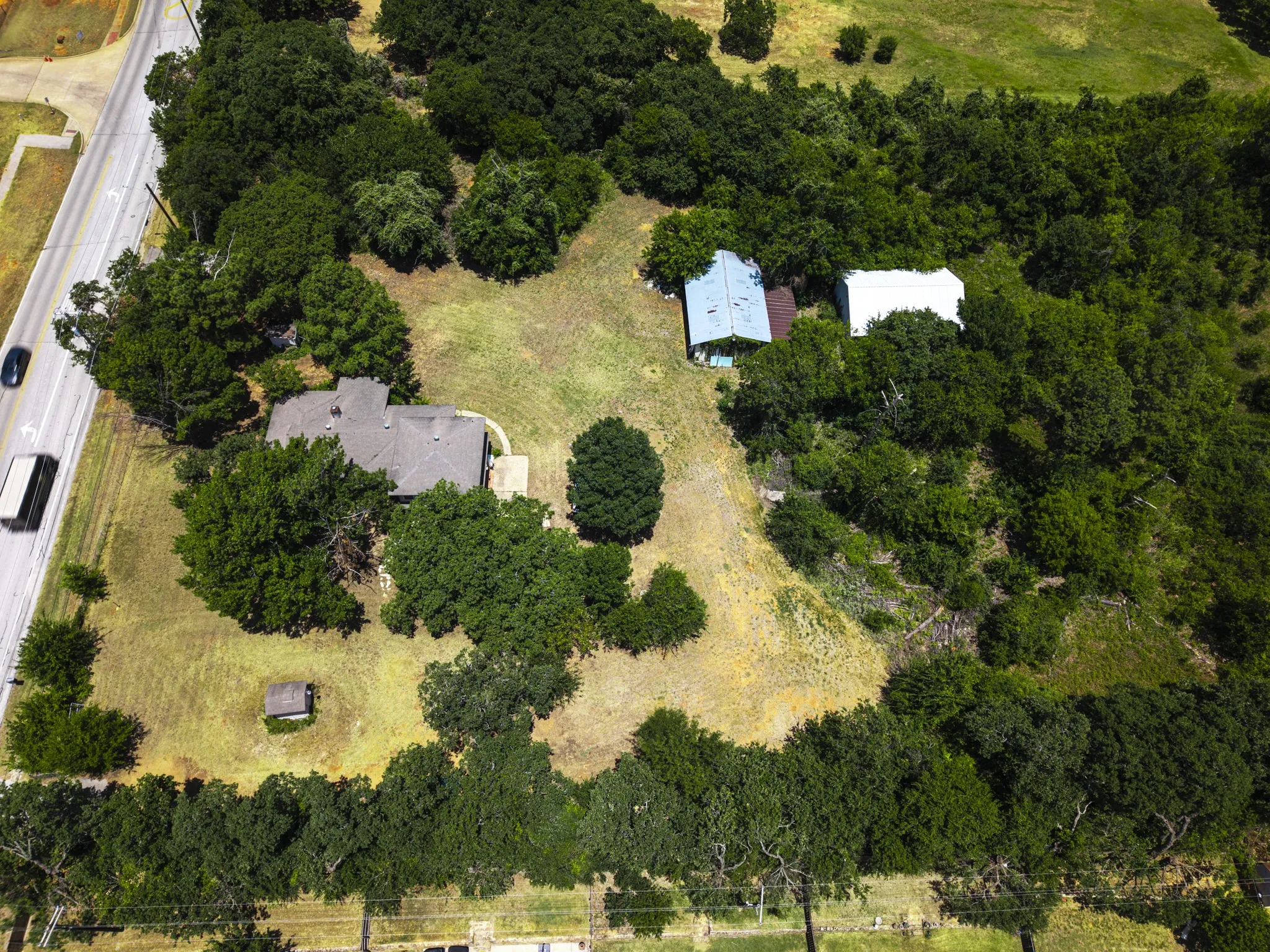 Expansive property featuring a main residence with a gray shingle roof, surrounded by mature trees and open land