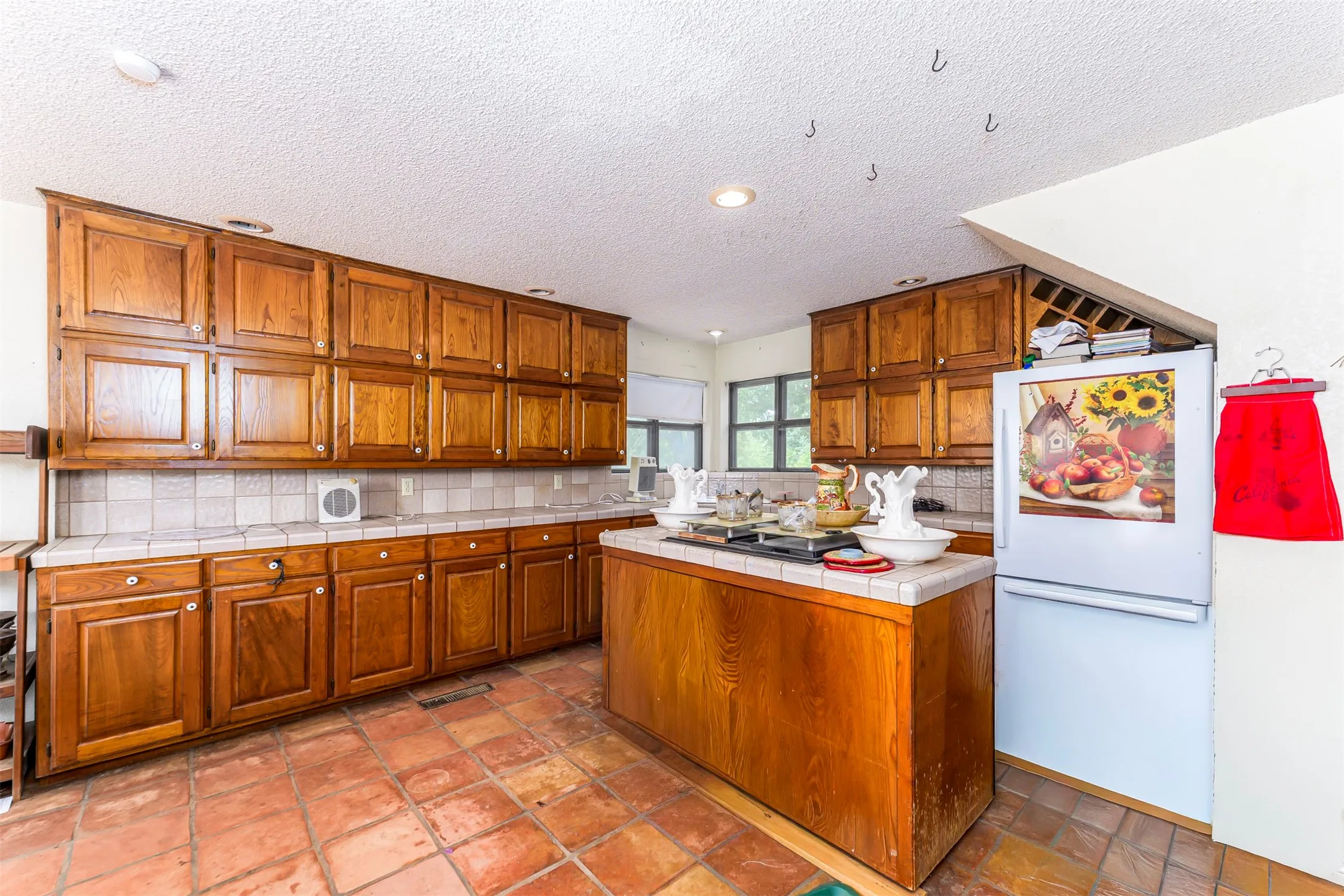 Kitchen featuring extensive wood cabinetry, tile countertops, and terra cotta style floor tiles