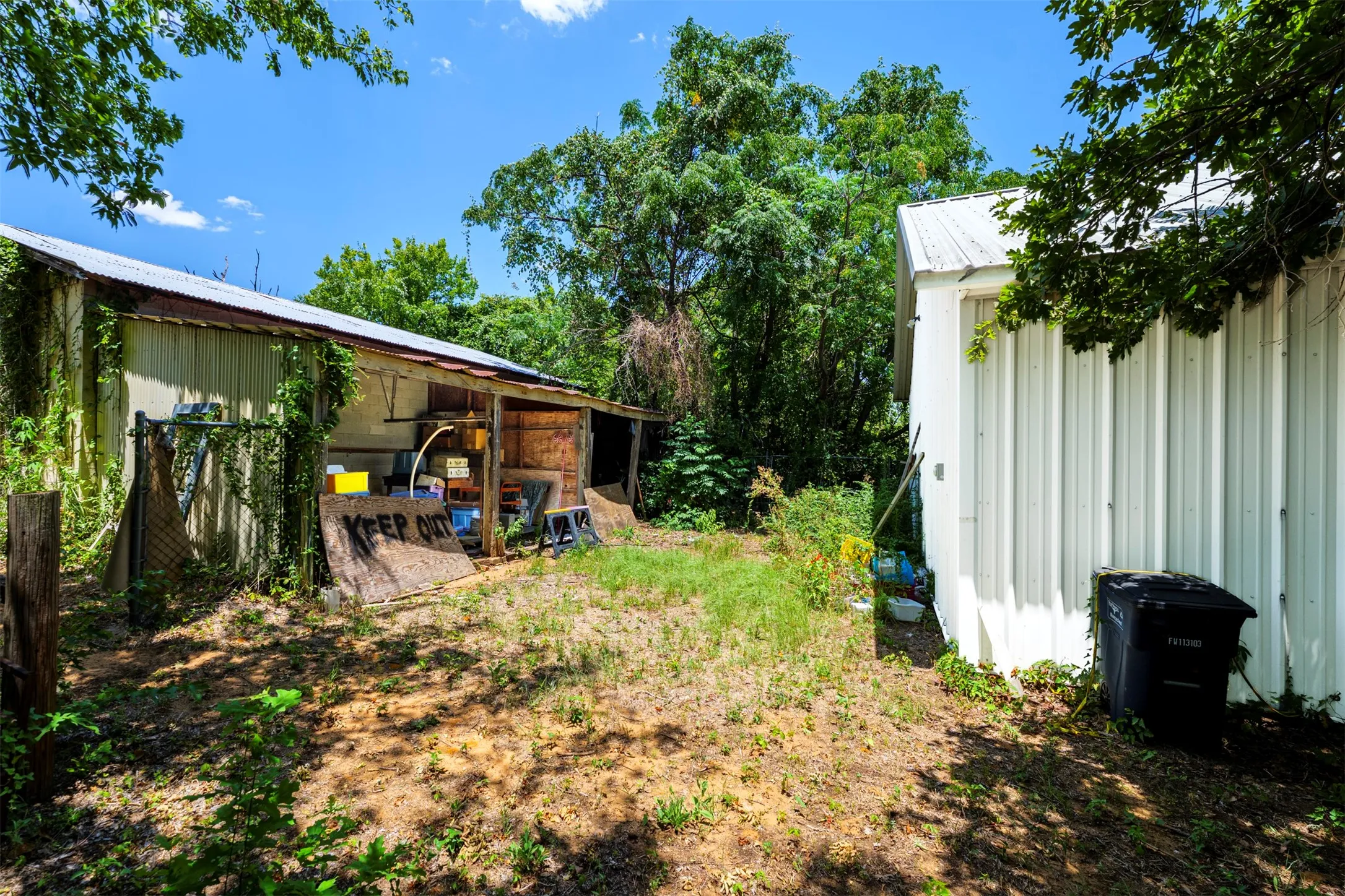 Two detached structures with corrugated metal roofing, surrounded by mature trees and natural landscaping