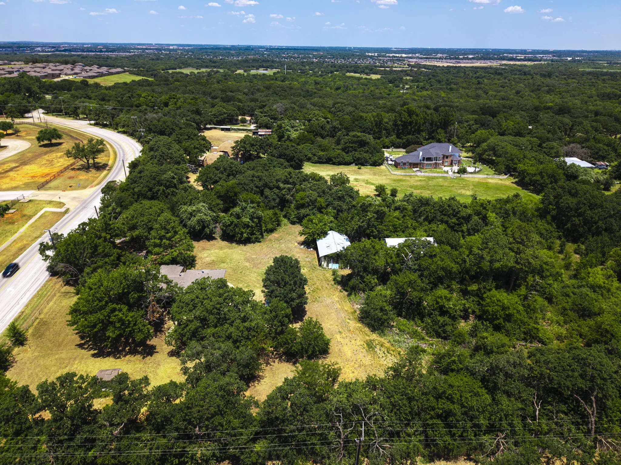 Expansive treed acreage featuring a paved road frontage, mature deciduous trees, and varied terrain