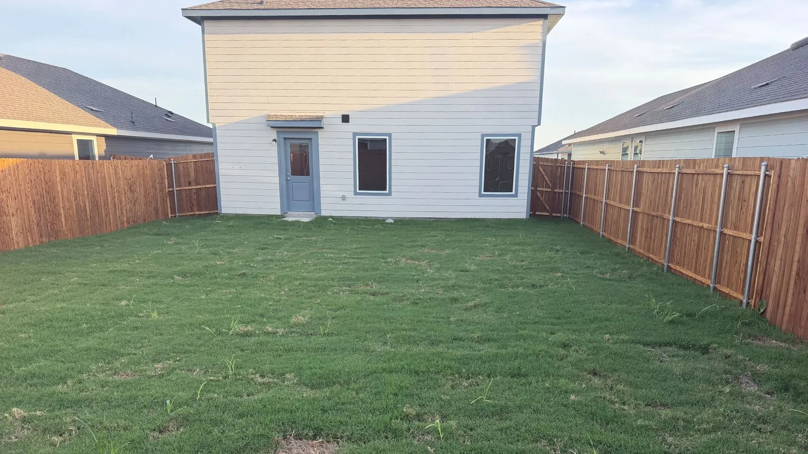 Expansive green yard featuring a privacy fence, rear entry door, and multiple windows