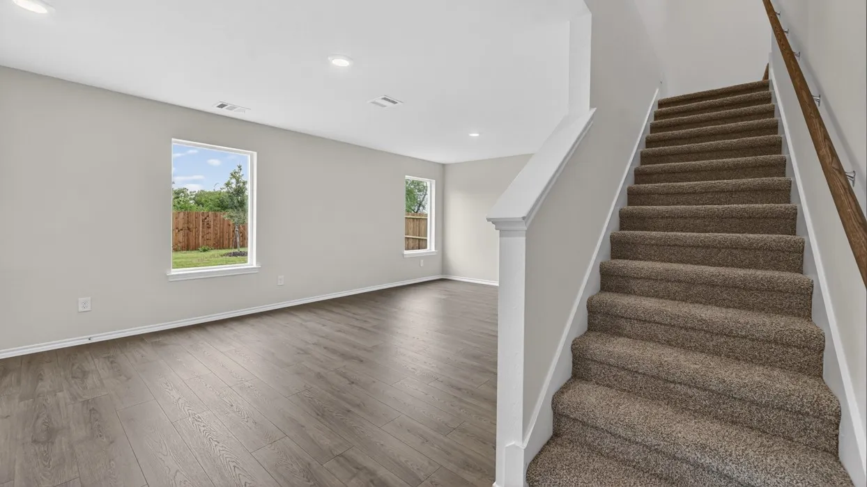 Spacious room featuring wood-finish flooring, two windows, recessed lighting, and a carpeted staircase with a wood handrail