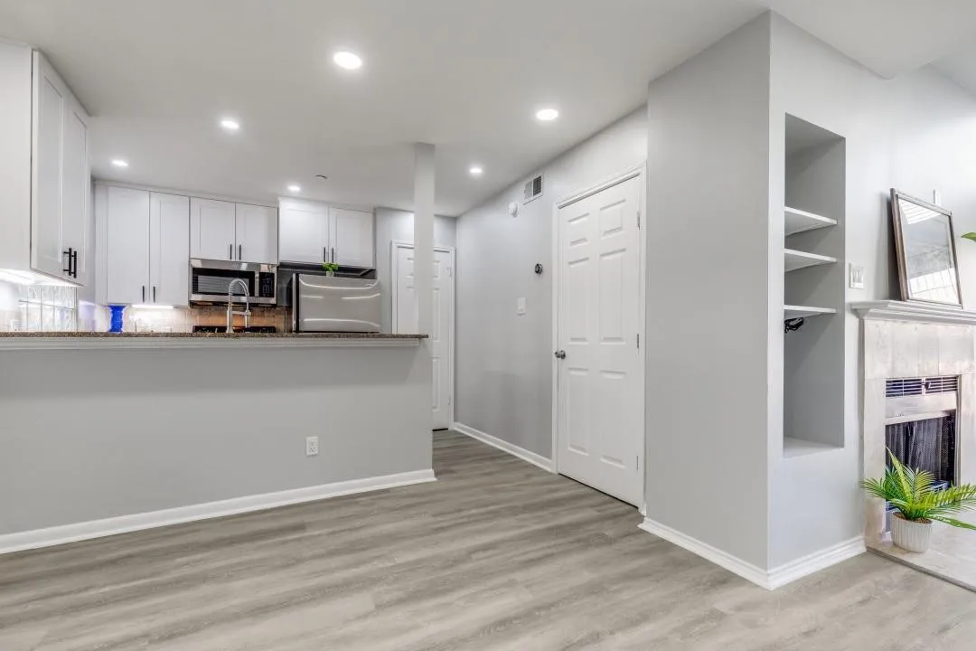 Open-concept living area featuring wood-finish flooring, recessed lighting, and a kitchen with white cabinetry and stainless steel appliances