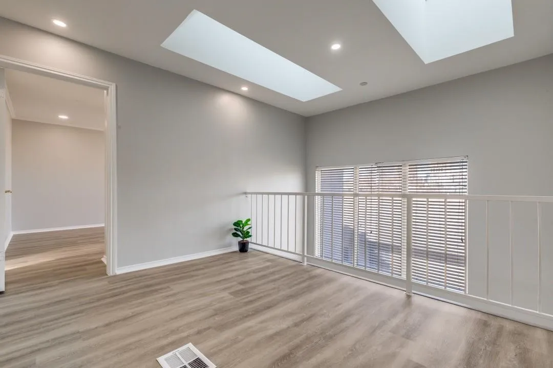 Loft area featuring two skylights, recessed lighting, wood-finish flooring, and white railing overlooking a window with horizontal blinds