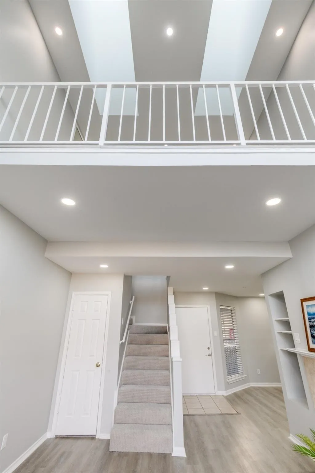 Two-story interior featuring a carpeted staircase, light wood-finish flooring, recessed lighting, and a second-story white metal railing