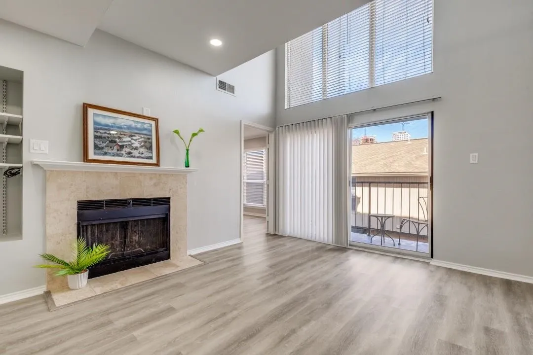 Living area featuring high ceilings, wood-finish flooring, a stone-surround fireplace, built-in shelving, and a sliding glass door opening to a private balcony