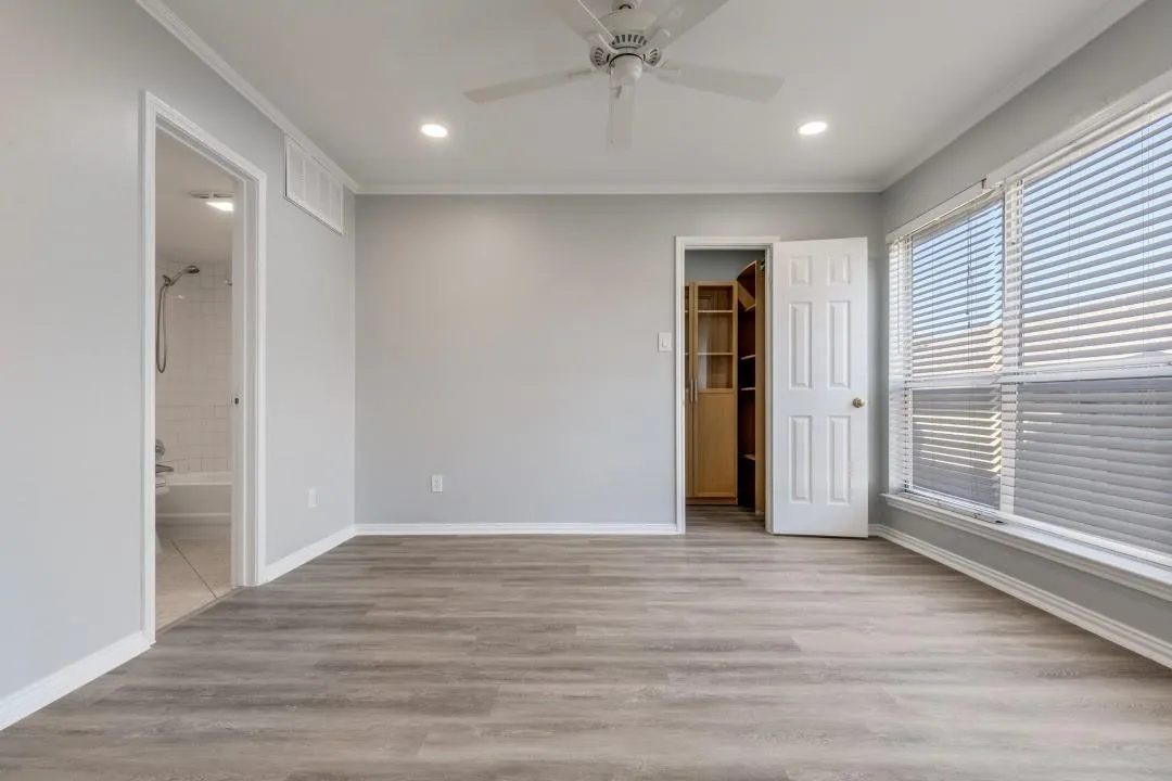 Spacious room featuring wood-finish flooring, ample natural light from large windows with blinds, a ceiling fan, recessed lighting, and a built-in closet with shelving