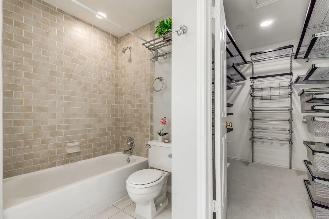 Full bathroom featuring a white porcelain tub and toilet, neutral subway tile surround, and tile flooring