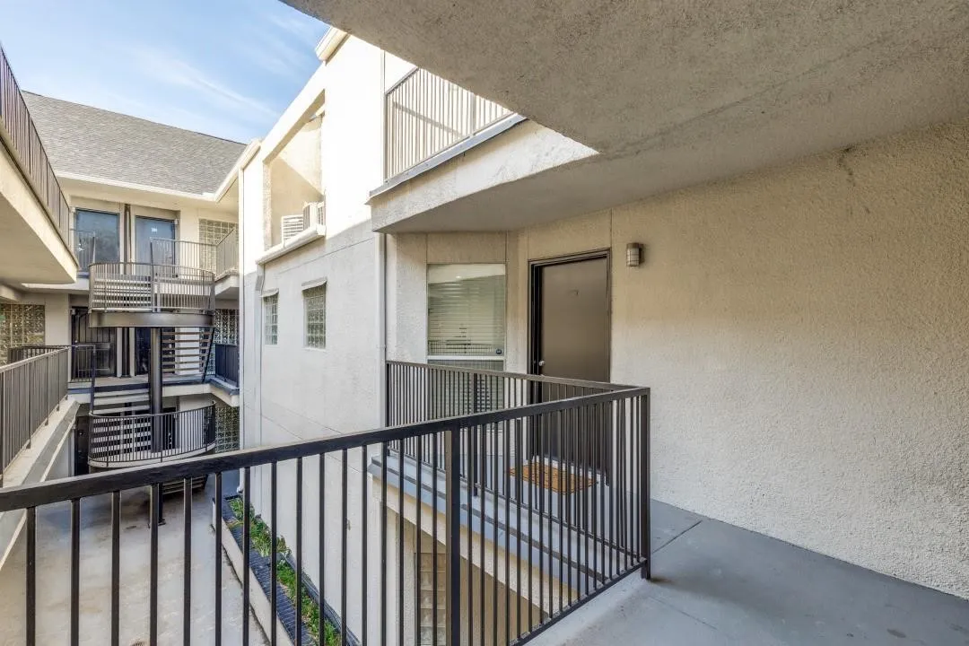 Exterior walkway with textured stucco walls, black metal railings, and a dark entry door