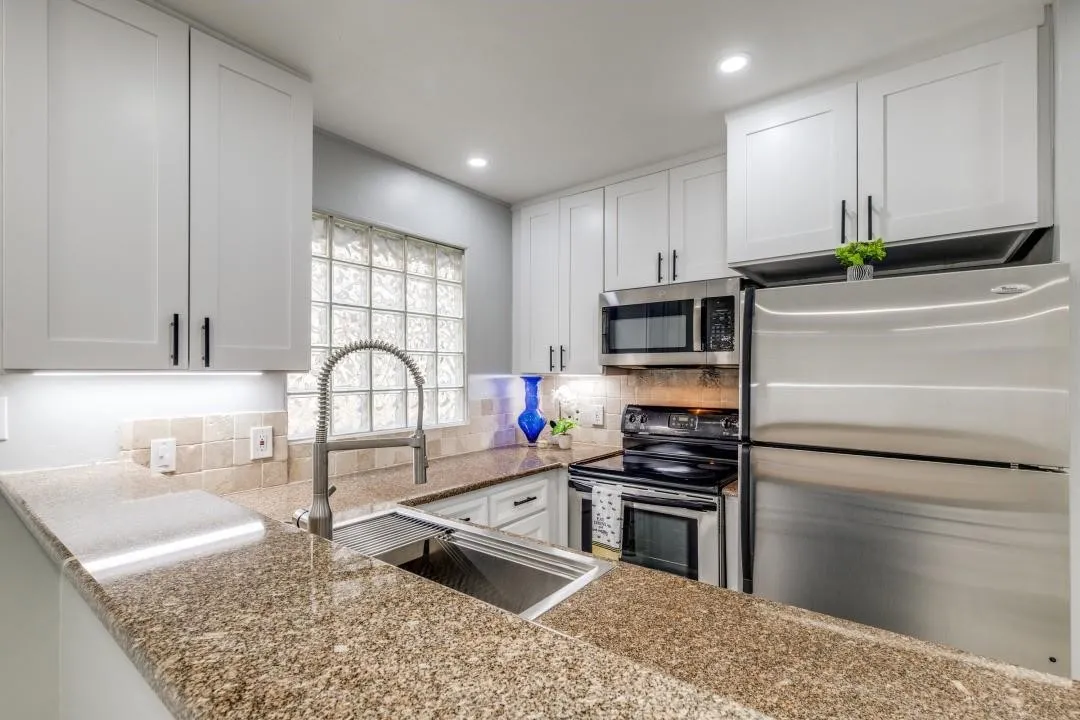 Well-appointed kitchen featuring granite countertops, white shaker cabinetry with matte black hardware, stainless steel appliances, and under-cabinet lighting