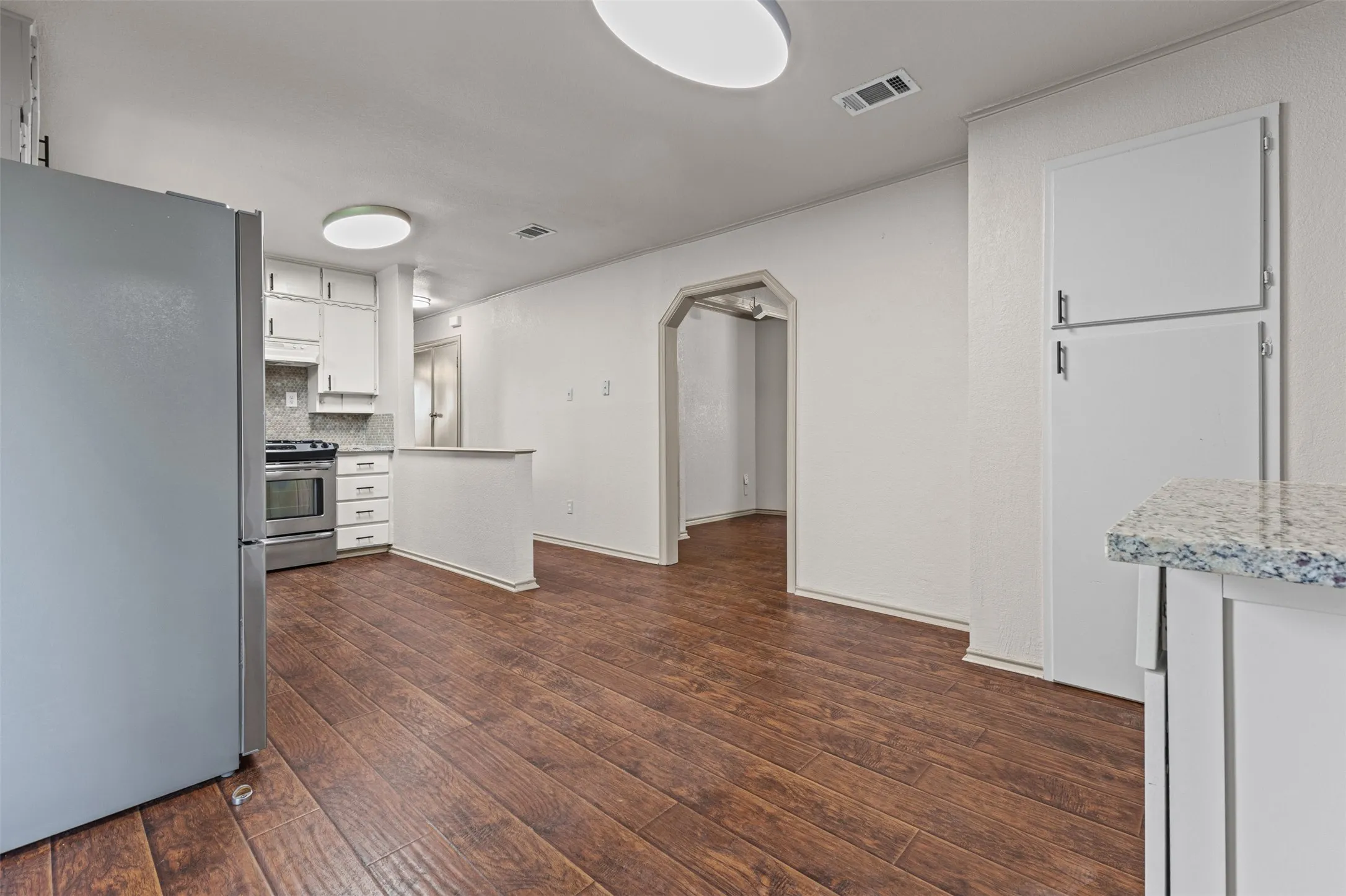 Kitchen and dining area featuring wood-finish flooring, white cabinetry, and stainless steel appliances