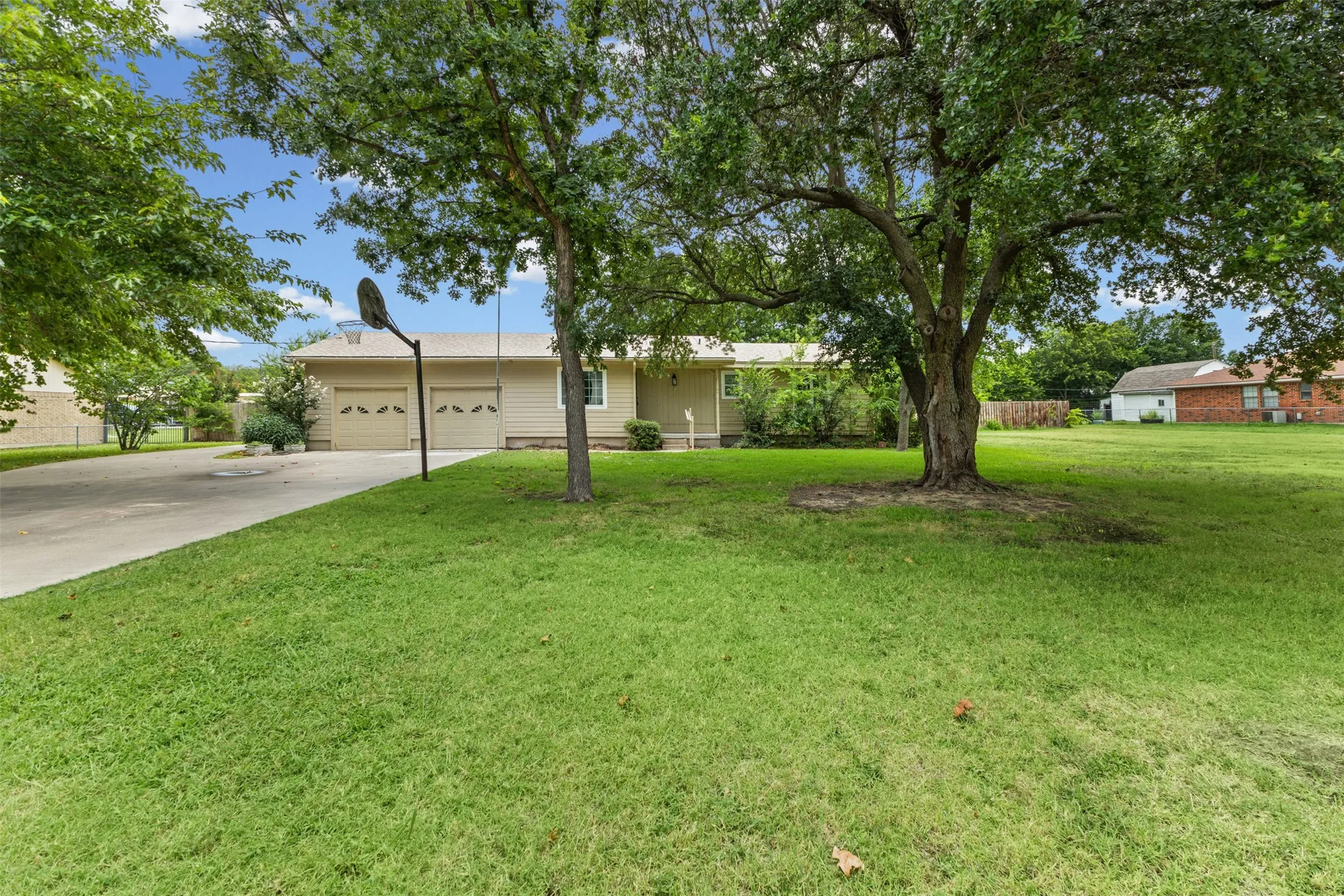 Expansive front lawn with mature trees and a long driveway leading to a two-car garage