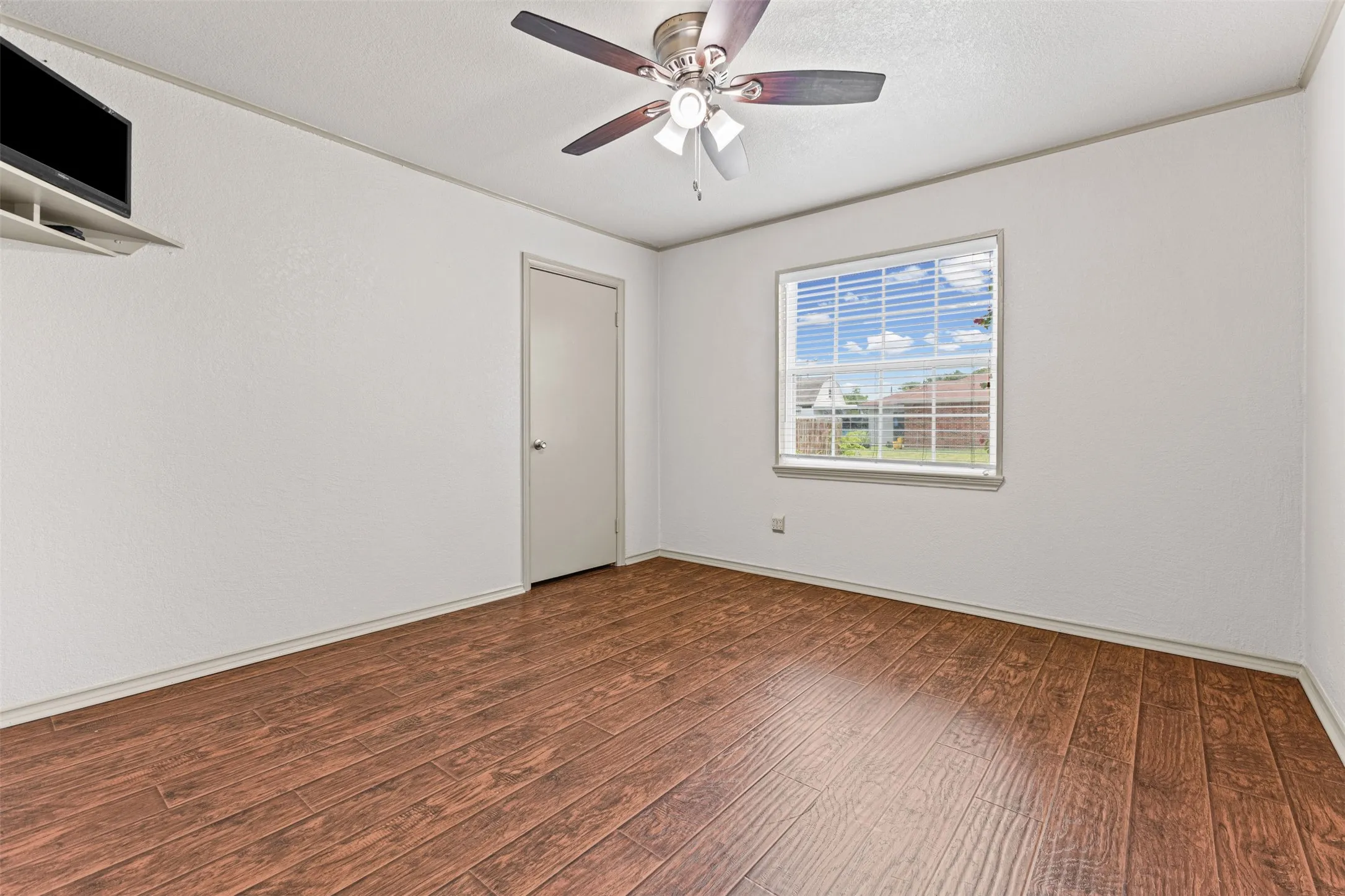 Spacious room featuring wood-finish flooring, a ceiling fan with integrated lighting, and a window with blinds