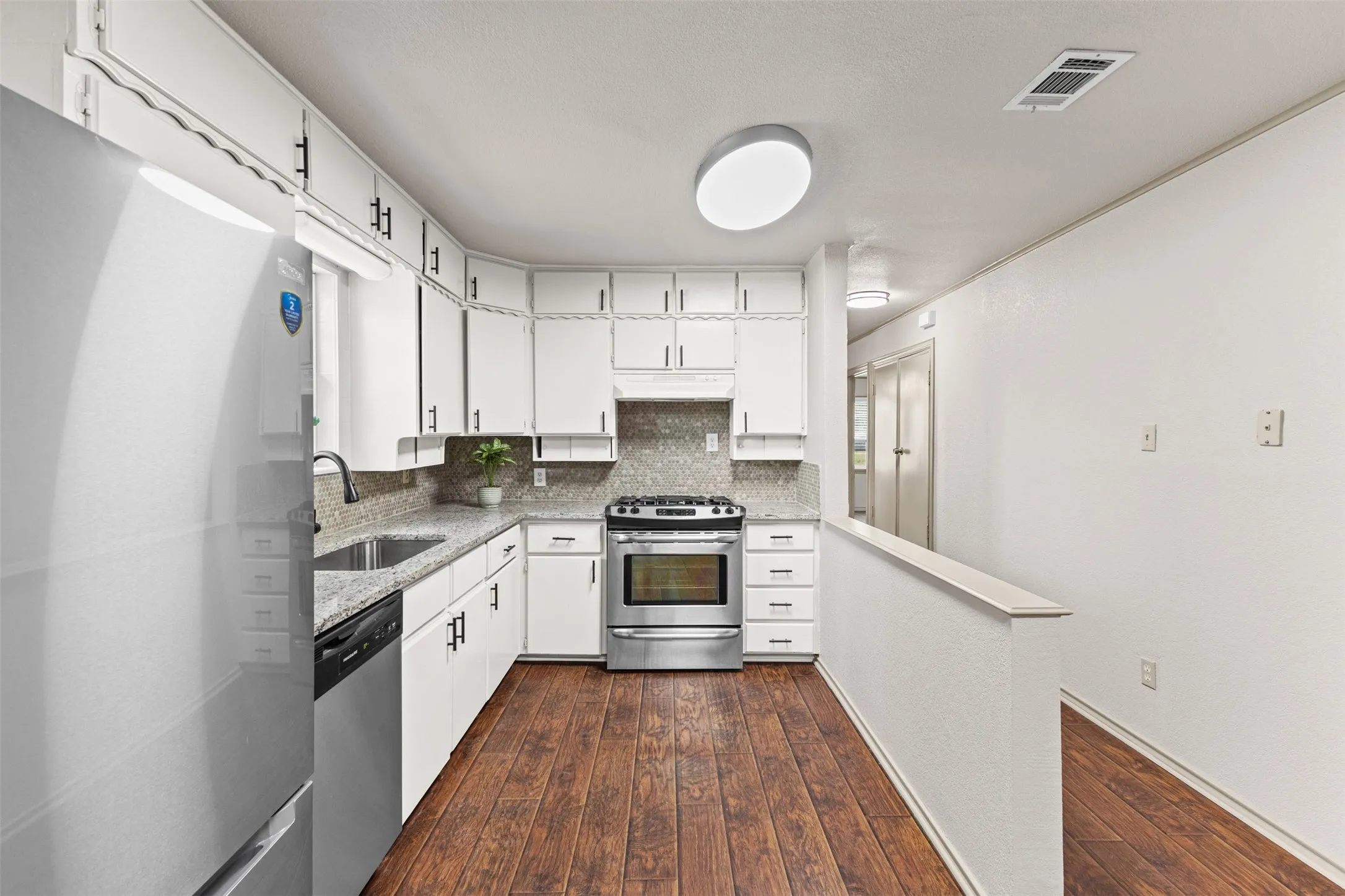 Kitchen featuring white cabinetry, granite-style countertops, stainless steel appliances, and wood-finish flooring