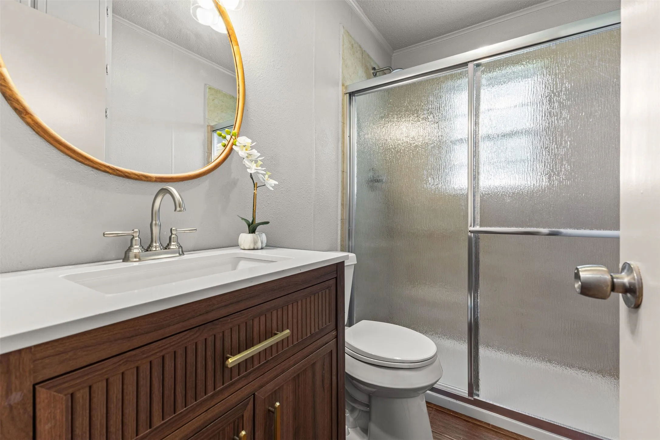 Bathroom featuring a wood-finish vanity with a white integrated sink, brushed nickel faucet, and a round wood-frame mirror