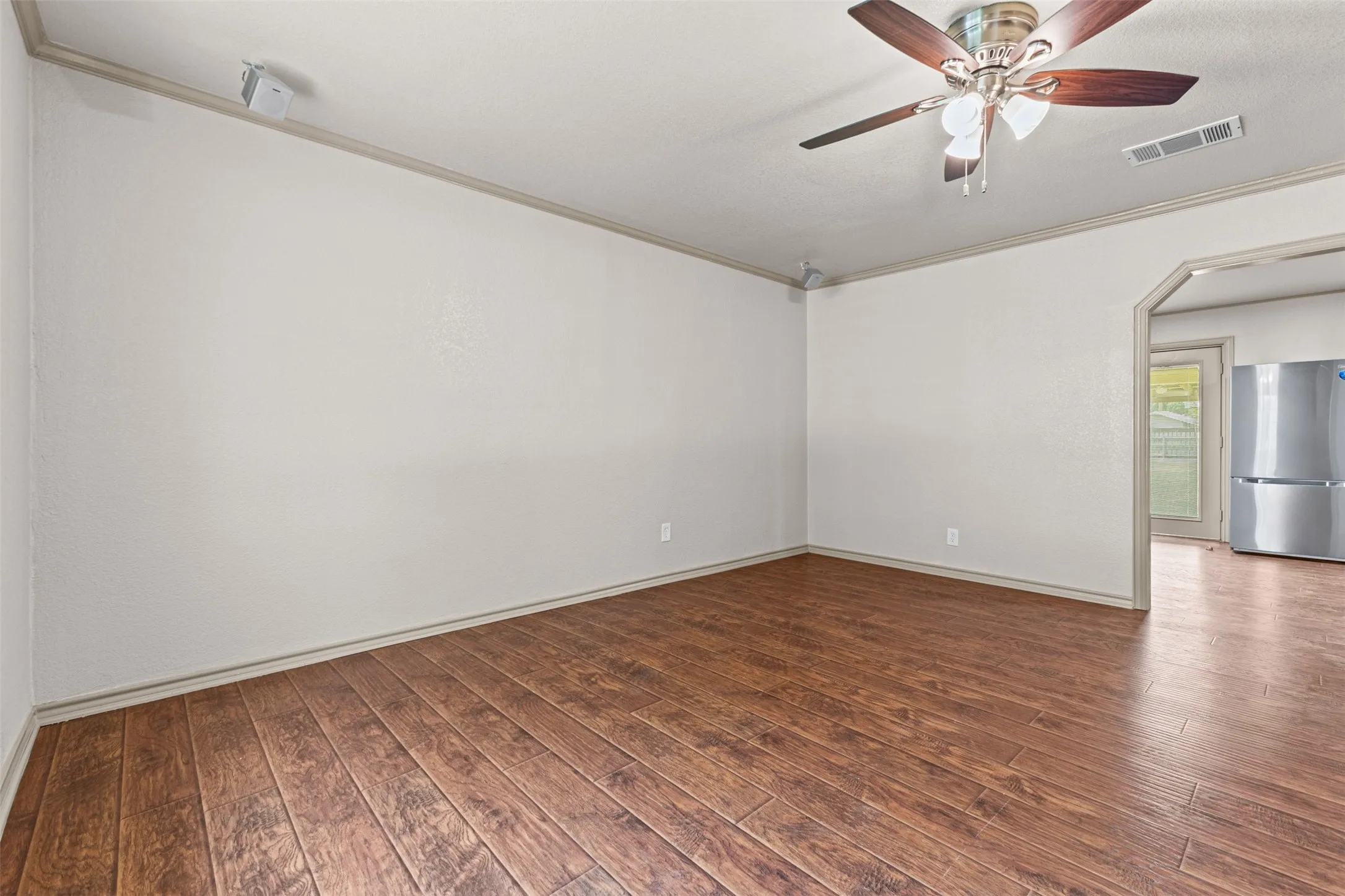 Spacious room featuring wood-finish flooring, a ceiling fan with integrated lighting, and crown molding