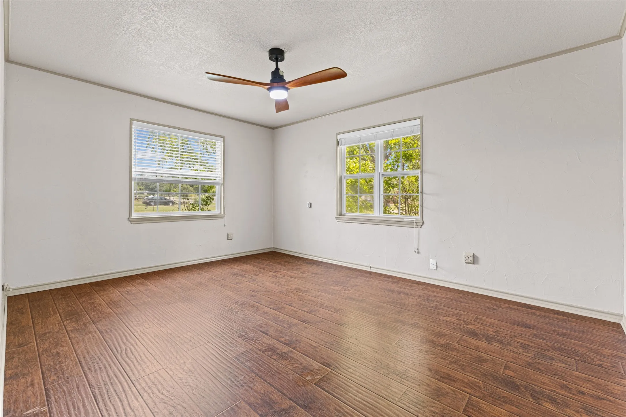 Spacious room featuring wood-finish flooring, white walls, and a ceiling fan with integrated lighting