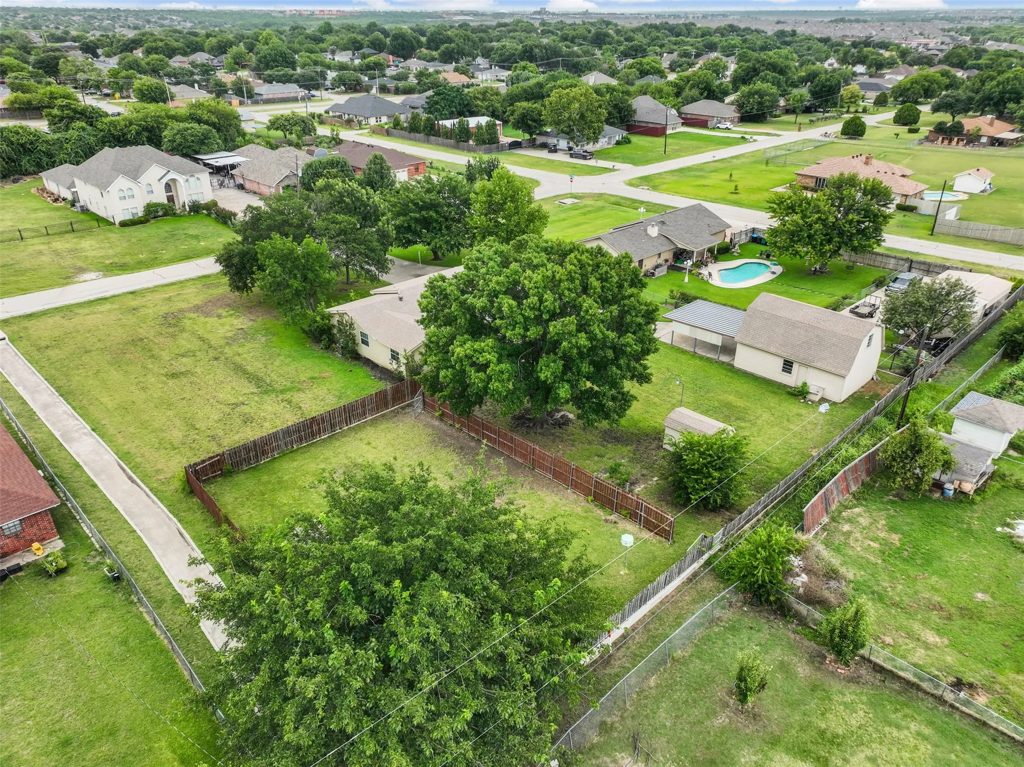 Expansive undeveloped lot featuring a long concrete driveway, perimeter fencing, and mature trees