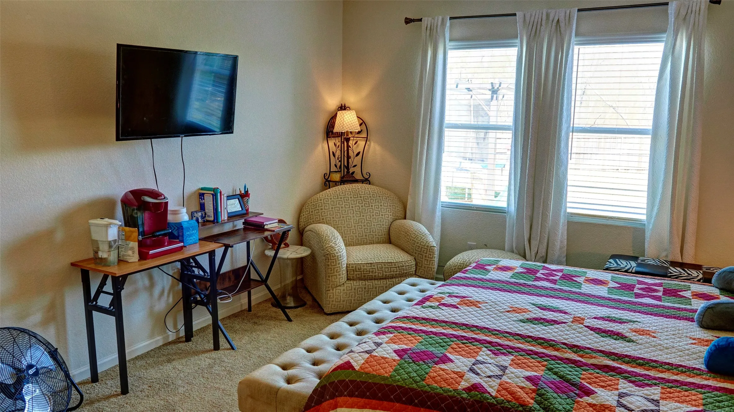 Wall-mounted television with visible wiring, carpeted flooring, corner accent lighting, and three tall windows with blinds