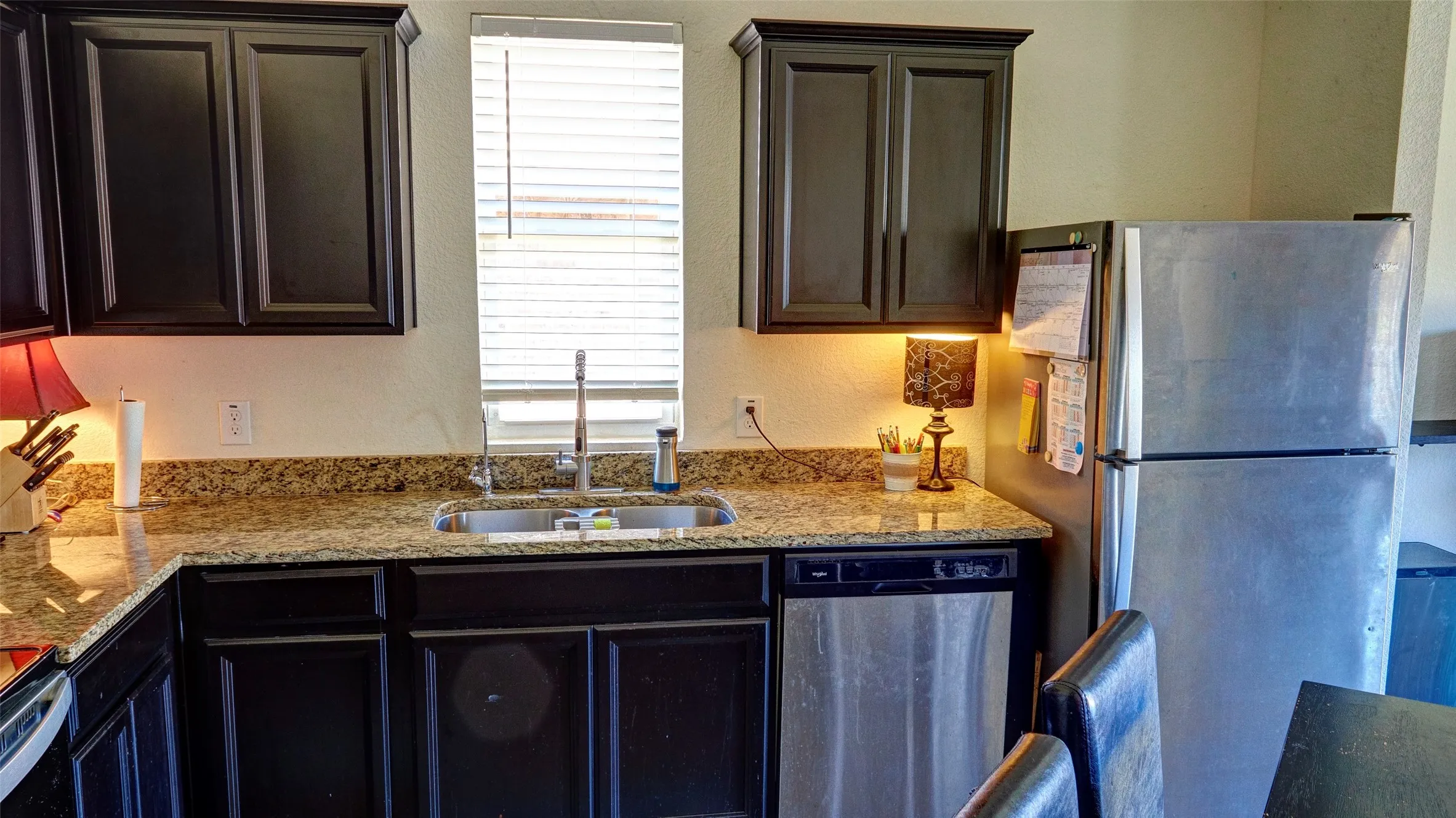 Dark wood-finish cabinetry, light-toned countertops, stainless steel appliances, and a double-basin sink with a chrome faucet