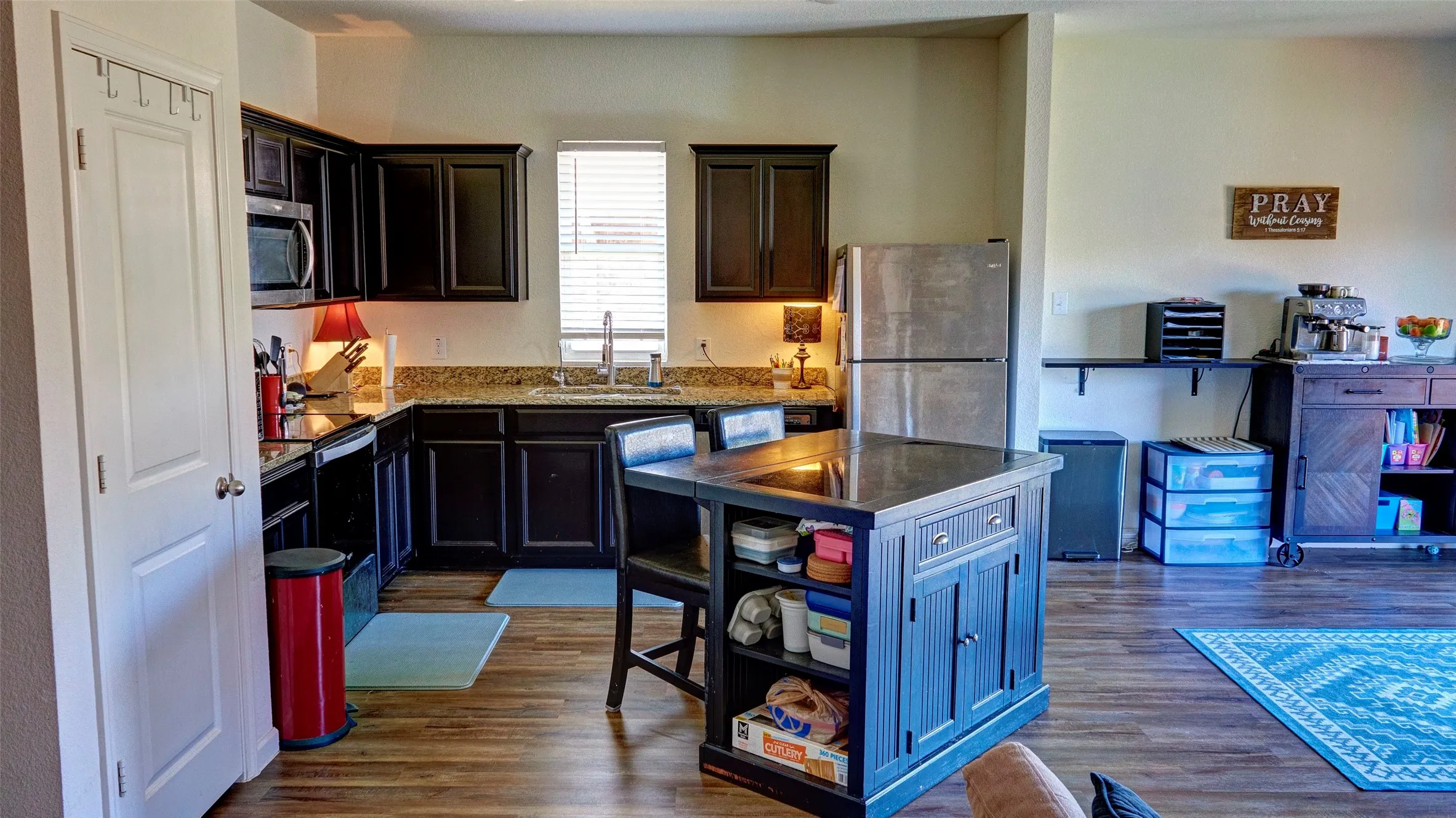 Kitchen featuring dark wood cabinetry, a central island with seating, stainless steel appliances, granite countertops, and wood-finish flooring