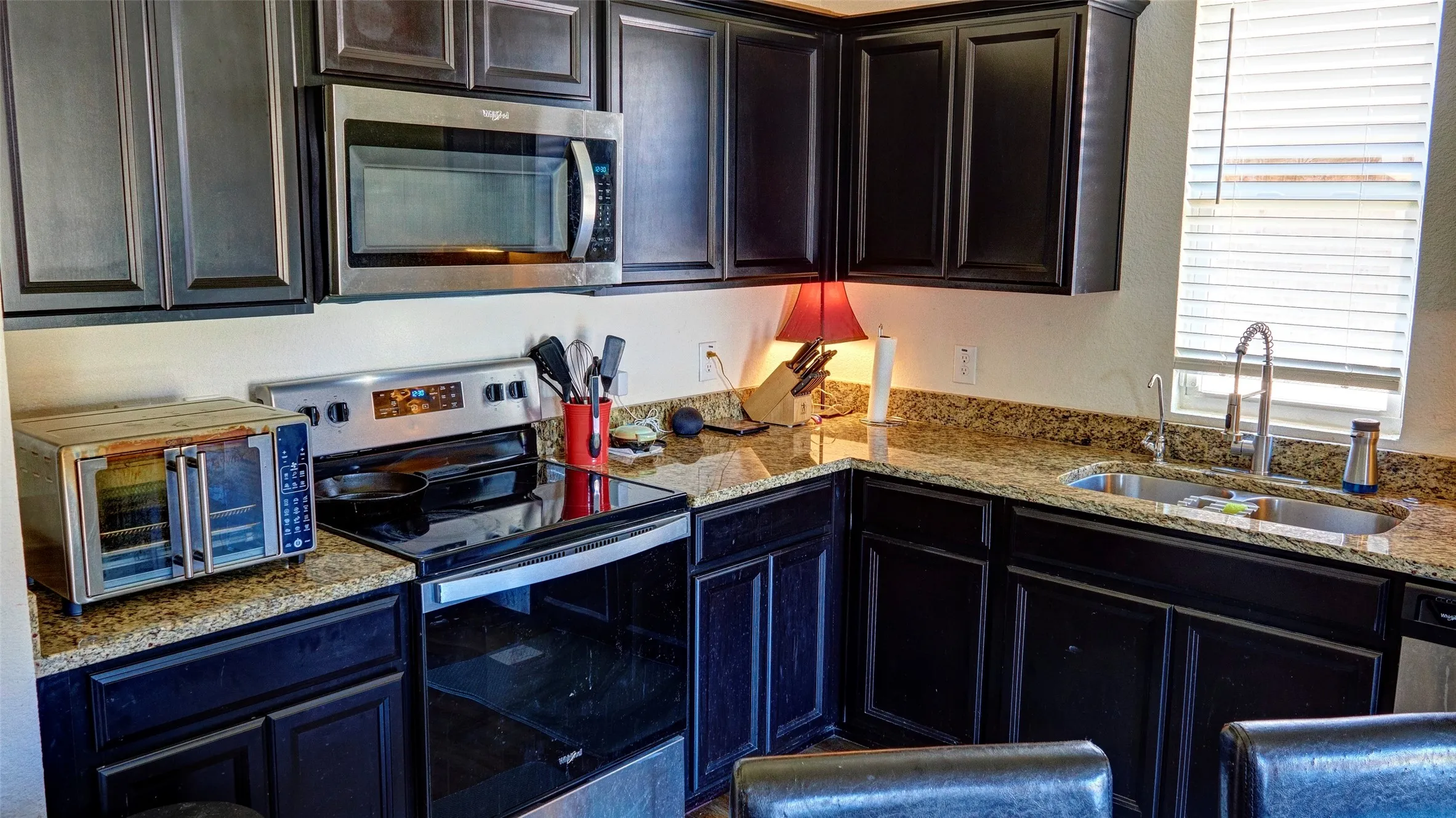 Kitchen featuring dark cabinetry, granite-style countertops, stainless steel appliances, and a double basin sink with a gooseneck faucet