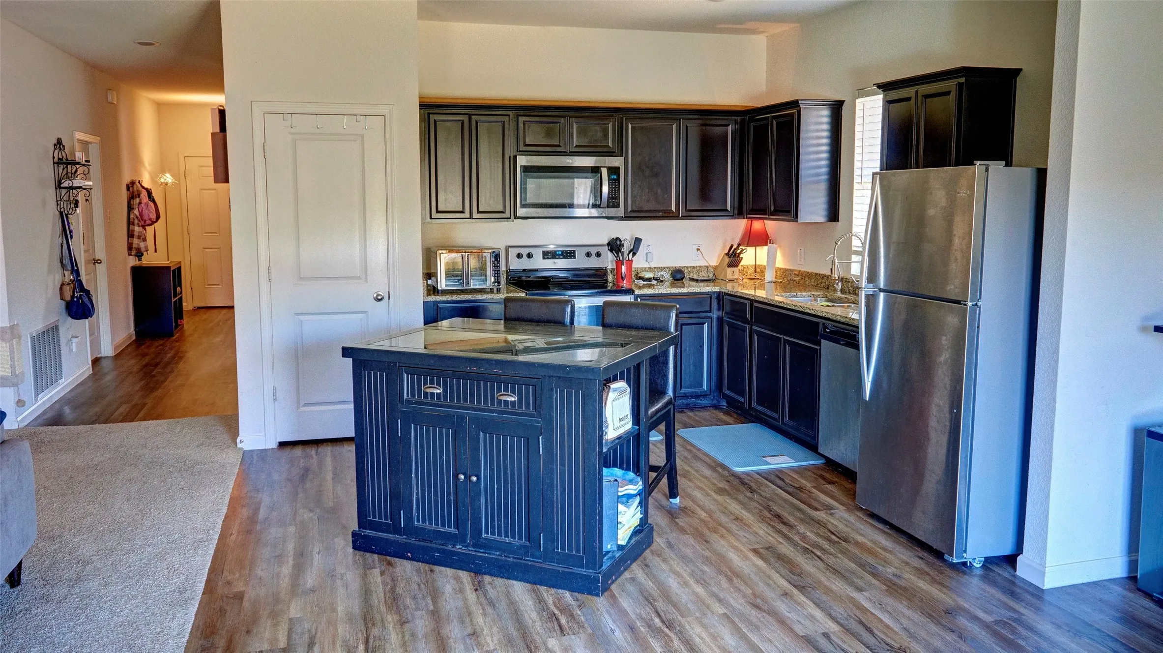 Kitchen featuring wood-finish flooring, dark cabinetry, stainless steel appliances, and a central island with a contrasting dark finish