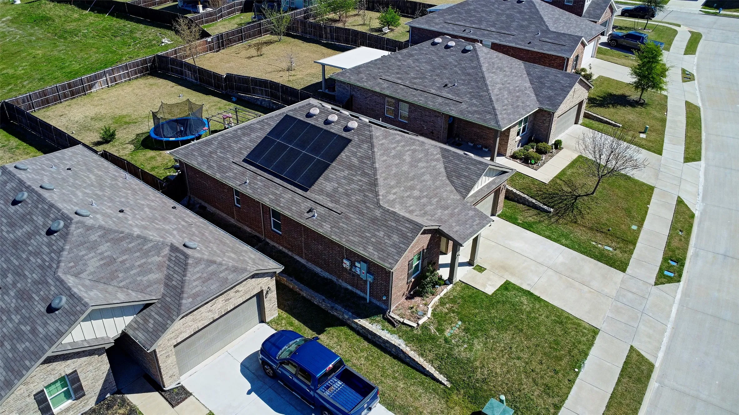 Brick exterior with an attached garage, featuring solar panels on the roof and a fenced backyard