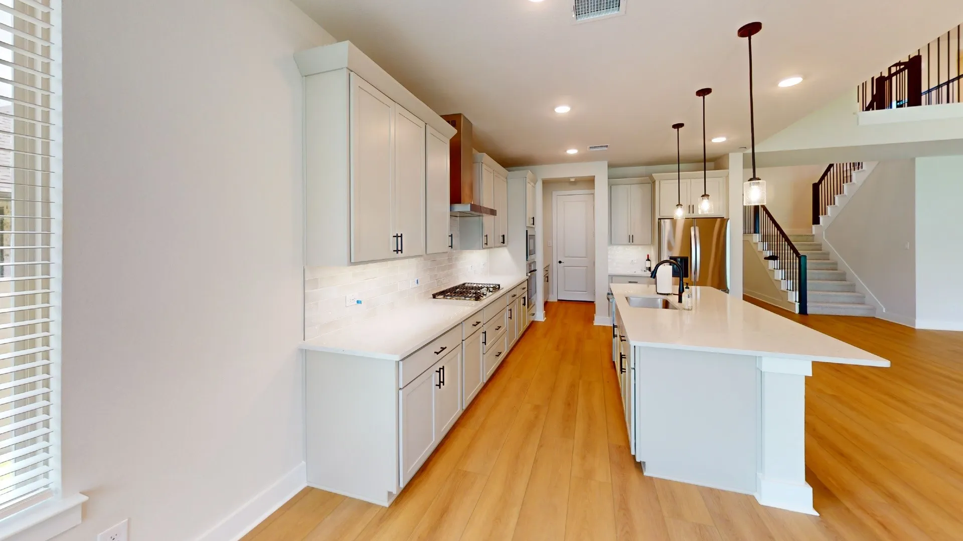 Open-concept kitchen with light wood-finish flooring, white cabinetry, a large kitchen island with pendant lighting, stainless steel appliances, and a gas range
