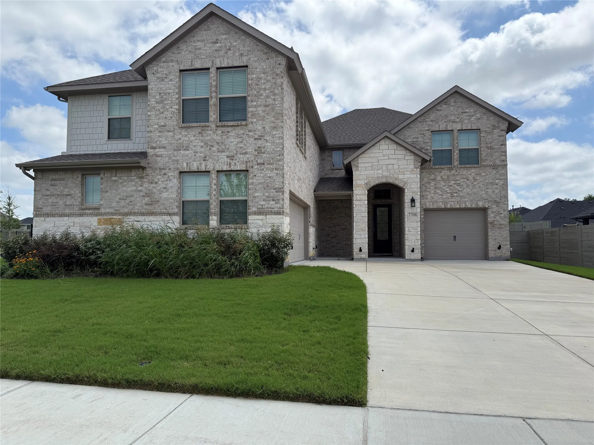 Two-story residence featuring a brick and stone facade with gabled rooflines, an arched entryway, and dual garage doors