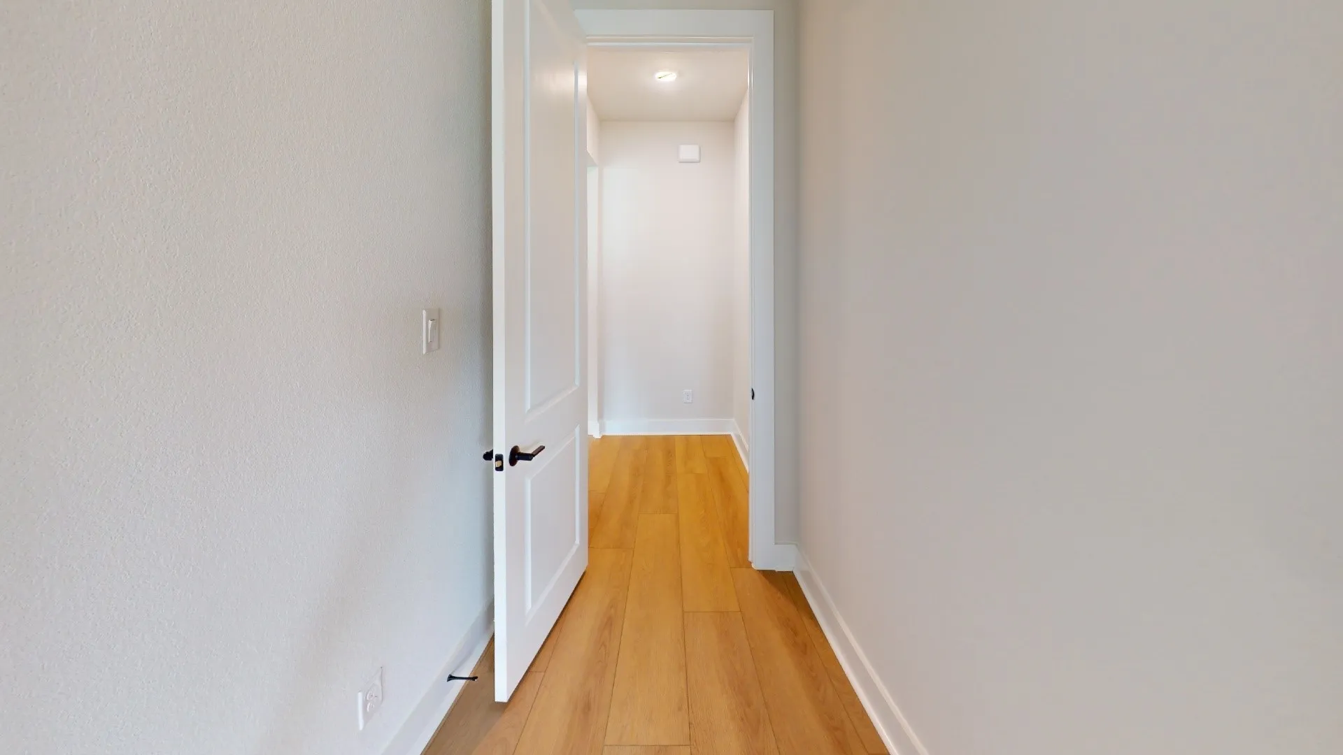 Hallway featuring light wood-finish flooring, white baseboards, and bright white walls