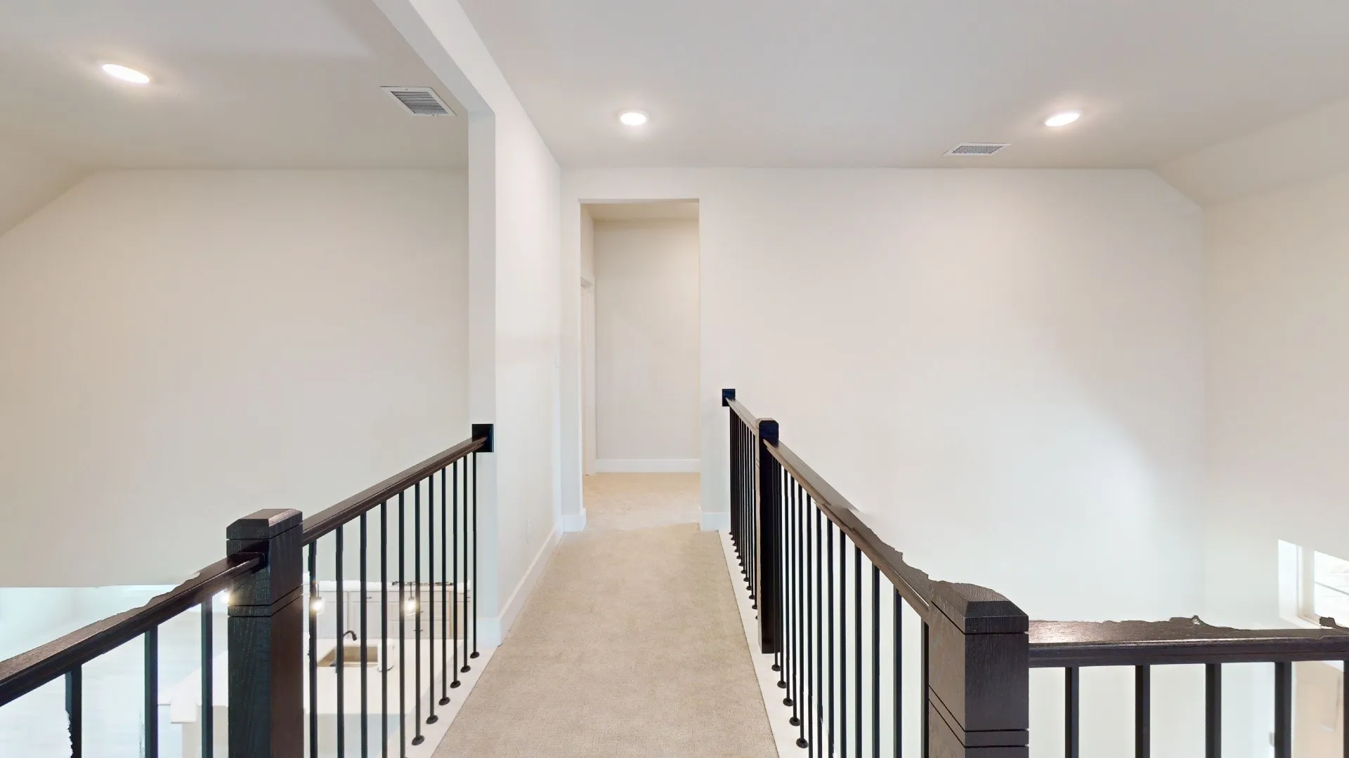 Carpeted hallway featuring a dark wood handrail with black iron balusters, recessed lighting, and white baseboards