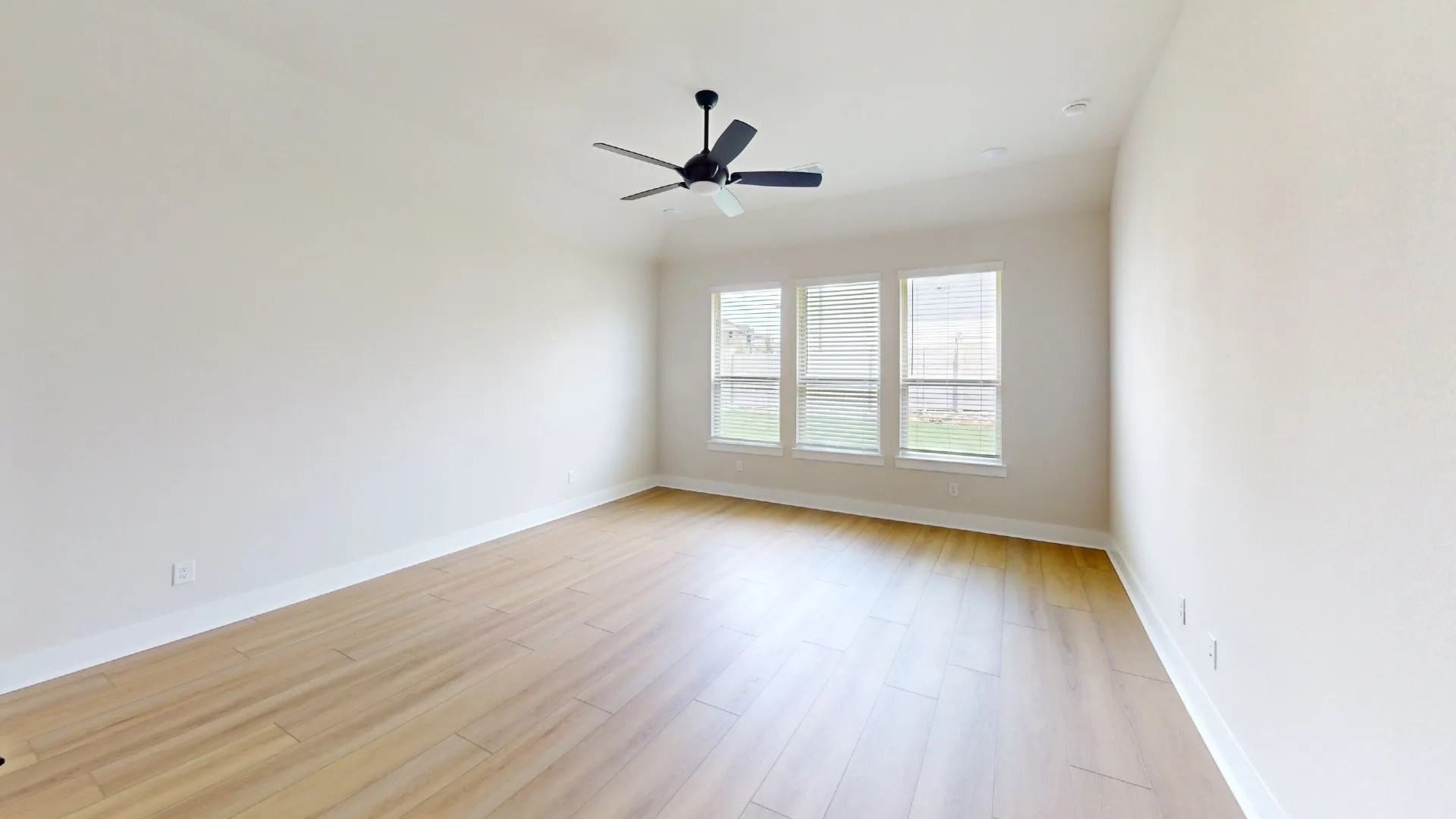 Bright room featuring light wood-finish flooring, white walls, and a black ceiling fan