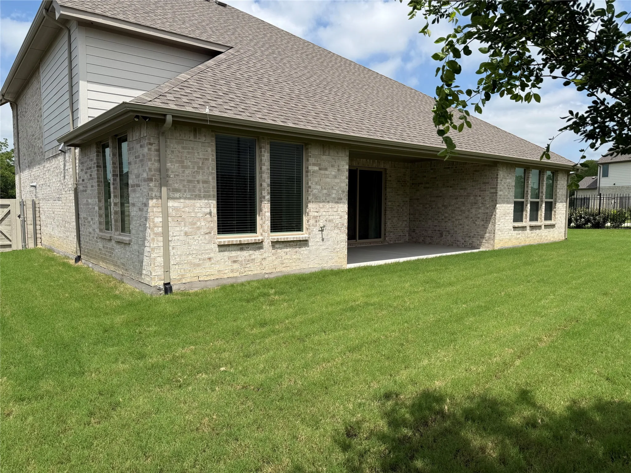Expansive green lawn surrounds a property featuring light-colored brick siding and a covered patio area