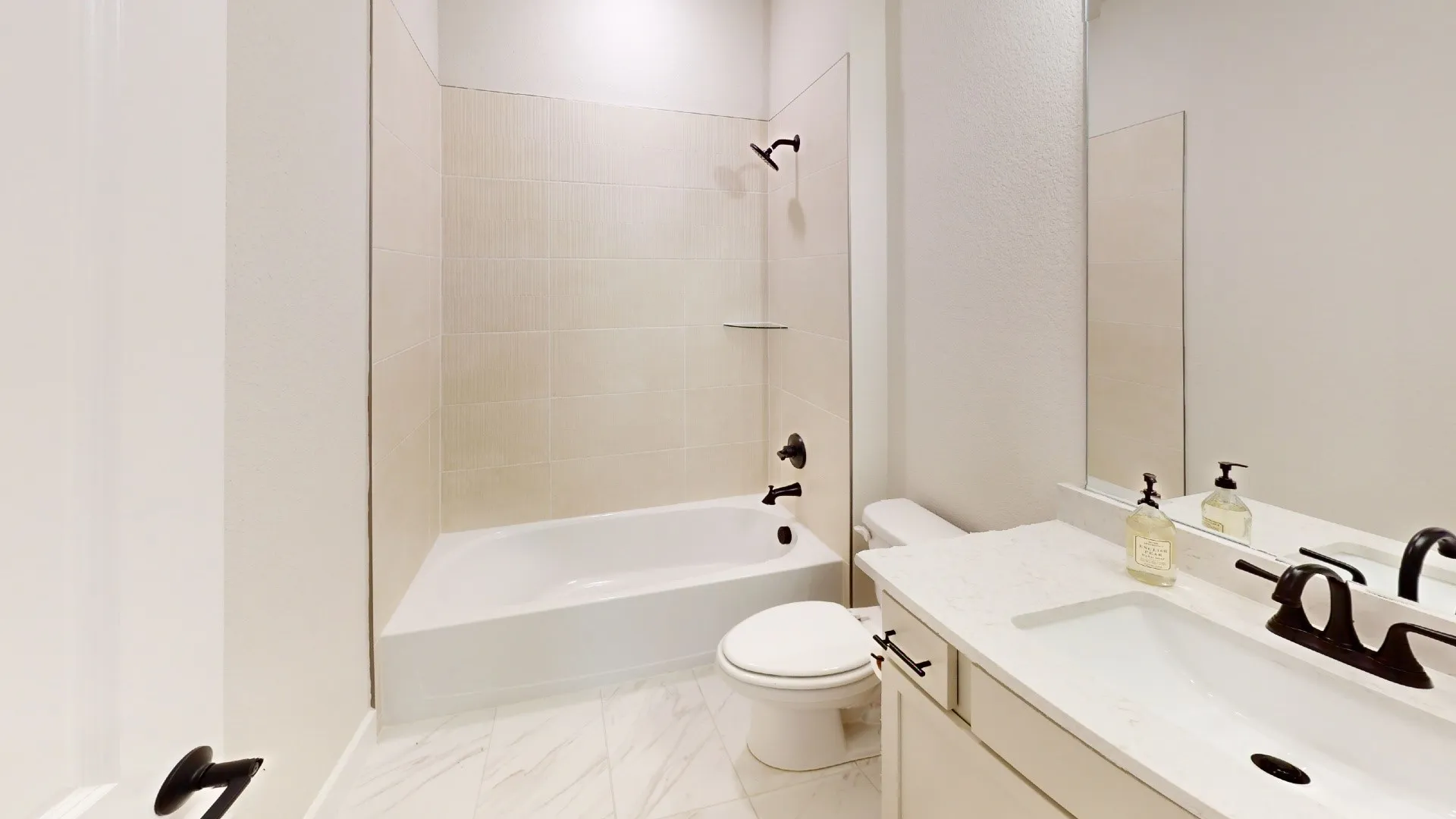 Bathroom featuring a single vanity with an integrated sink, a large mirror, a toilet, and a combination tub and shower with tile surround