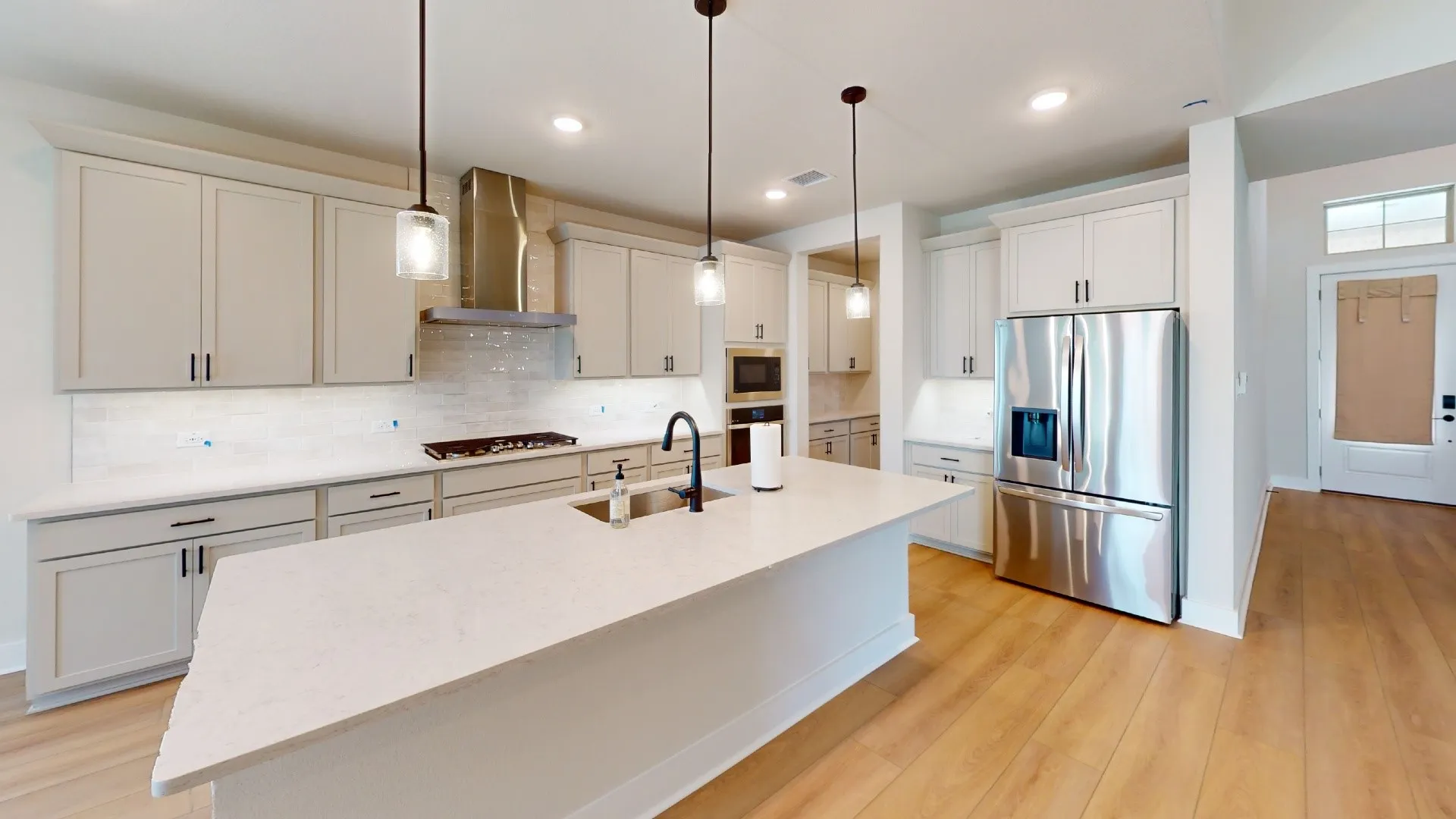 Modern kitchen featuring a large central island, light cabinetry, stainless steel appliances, wood-finish flooring, and pendant lighting