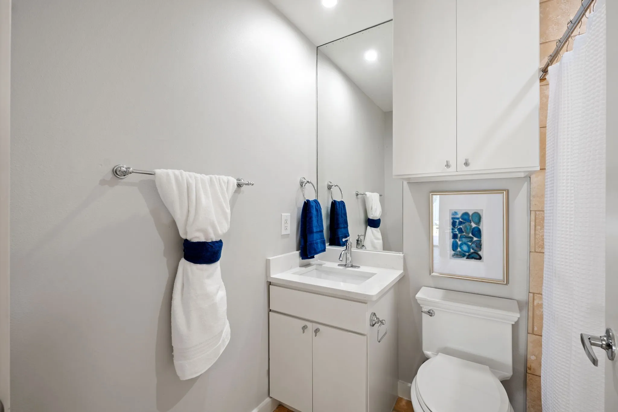 Bathroom featuring a vanity with a white countertop and undermount sink, a large wall-mounted mirror, white cabinetry, and a toilet